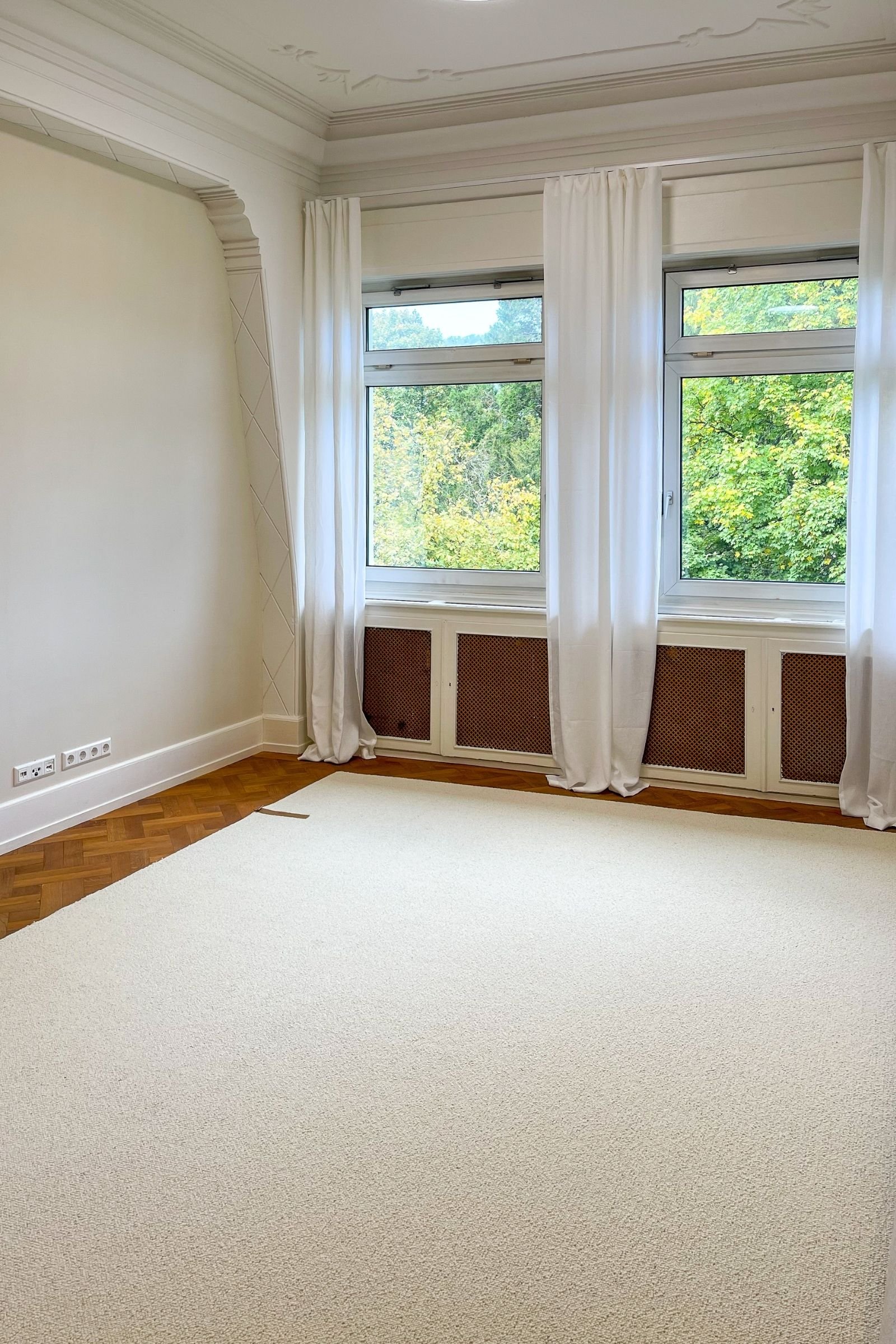 Heller Teppichboden auf dem Eichenparkett im Altbau-Wohnzimmer mit Fenstern