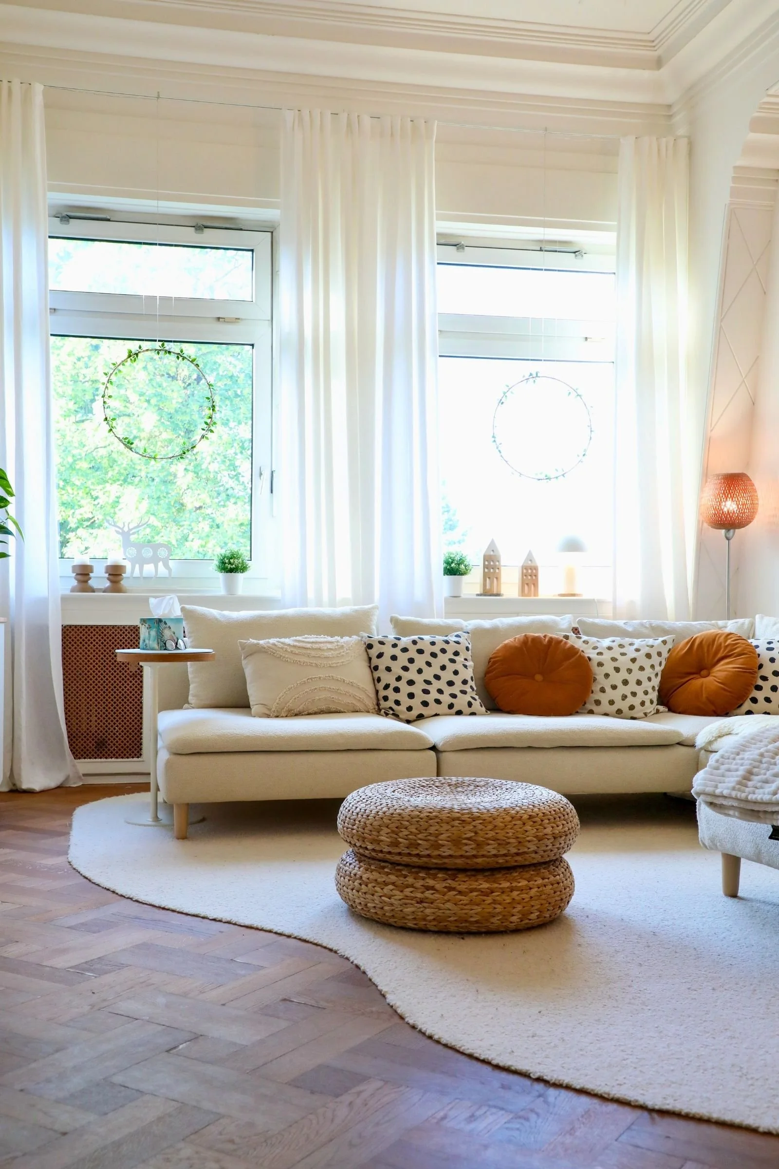 Creme Sofa mit organischem Wollteppich, Kissen und Fenstern mit weißen Vorhängen