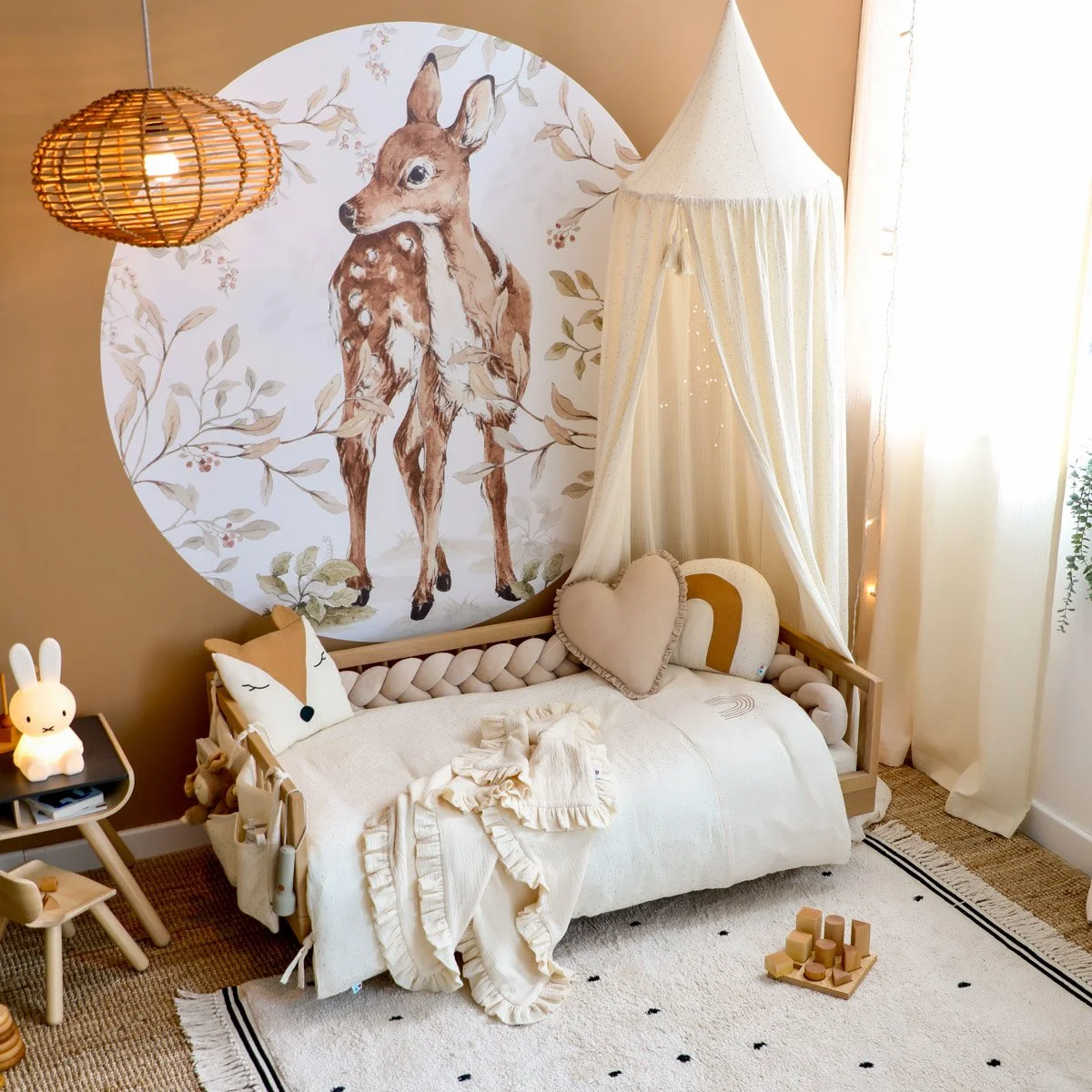 Kinderbett mit weichen Textilien vor braunen Wand mit Reh-Wandtattoo