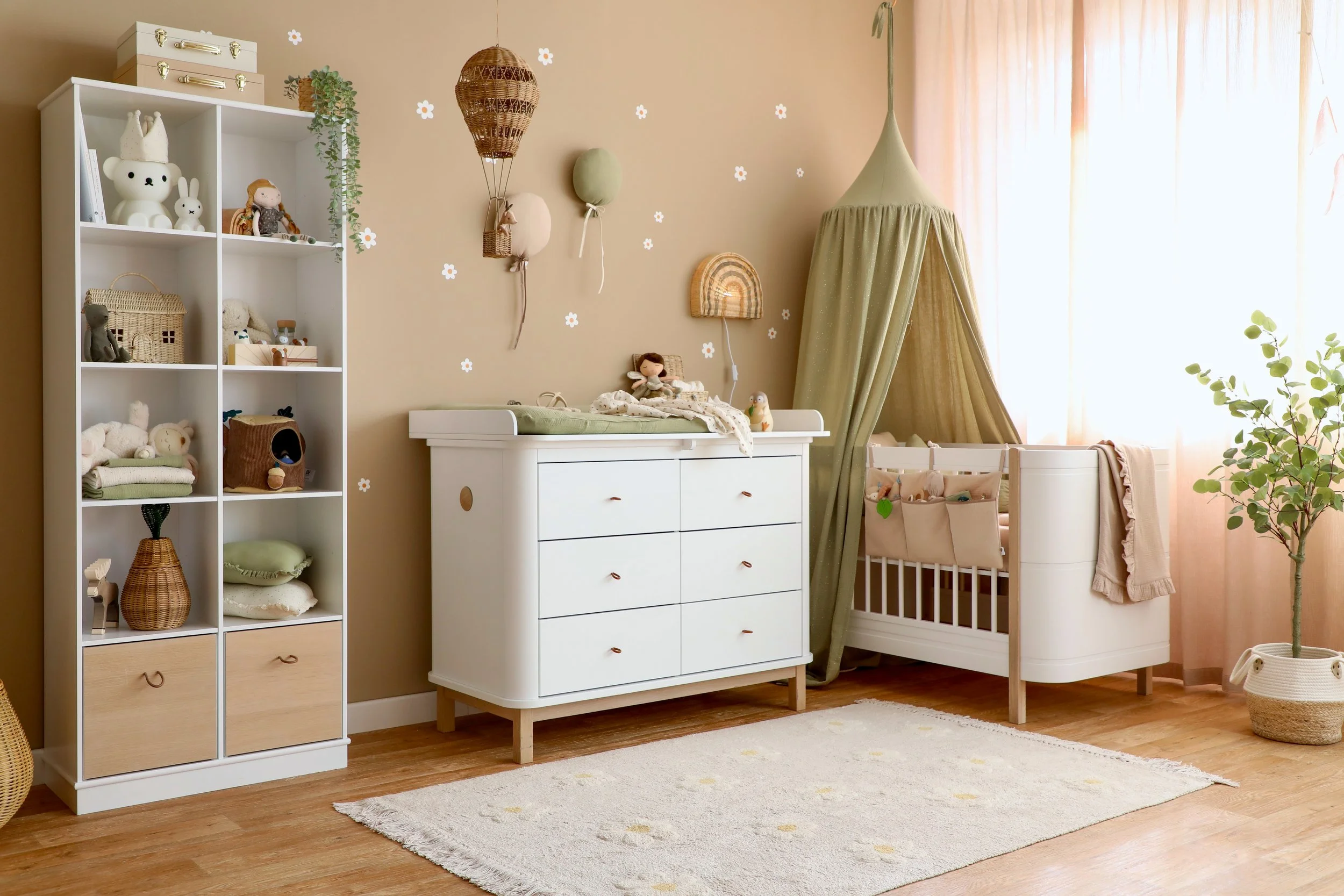 Babybett mit grünem Betthimmel, Regal und Wickelkommode vor einer beigen Wand
