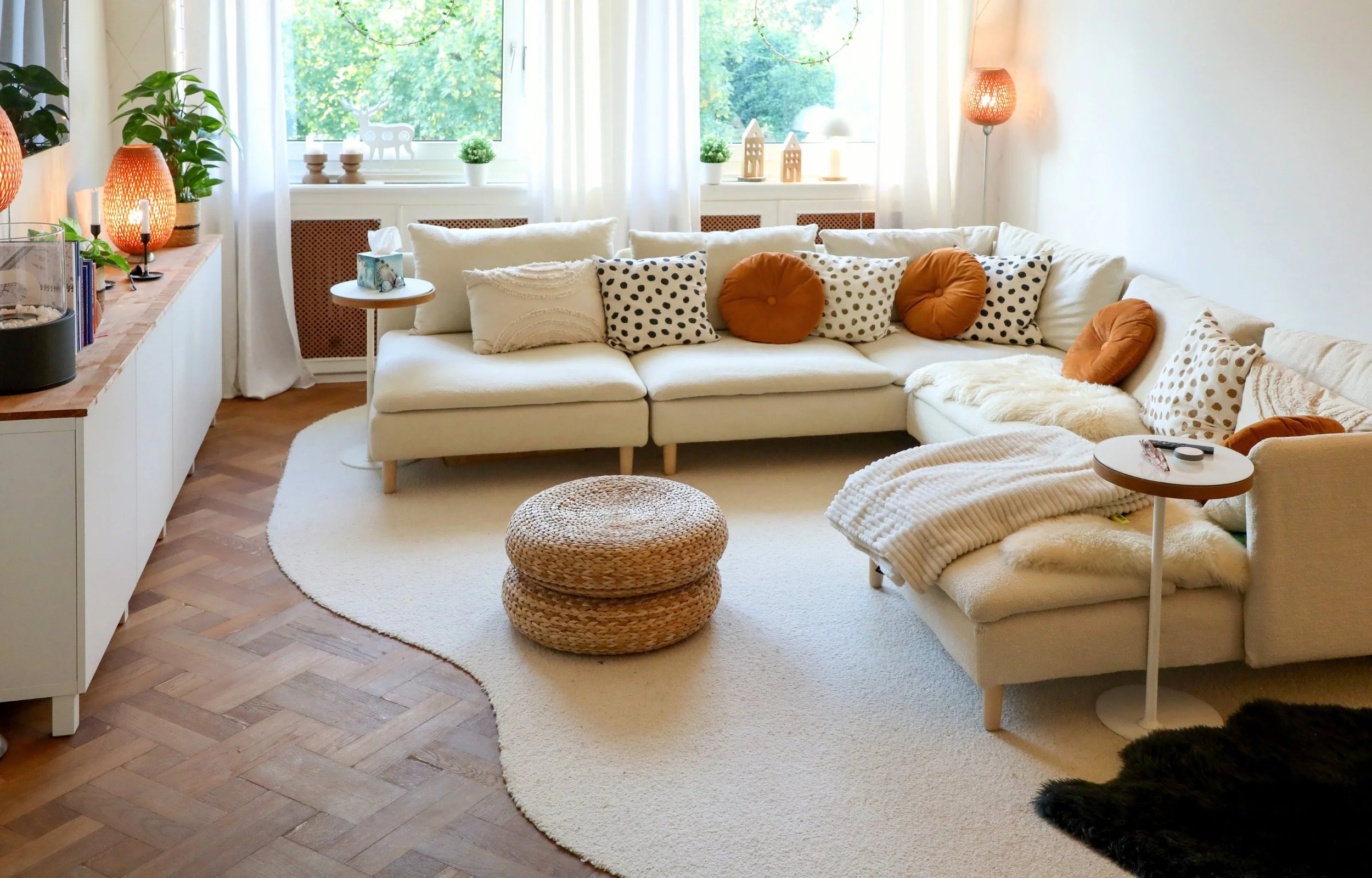 Beiges Sofa mit Kissen, hellem organischen Teppich, Fenster, Lampen und Deko