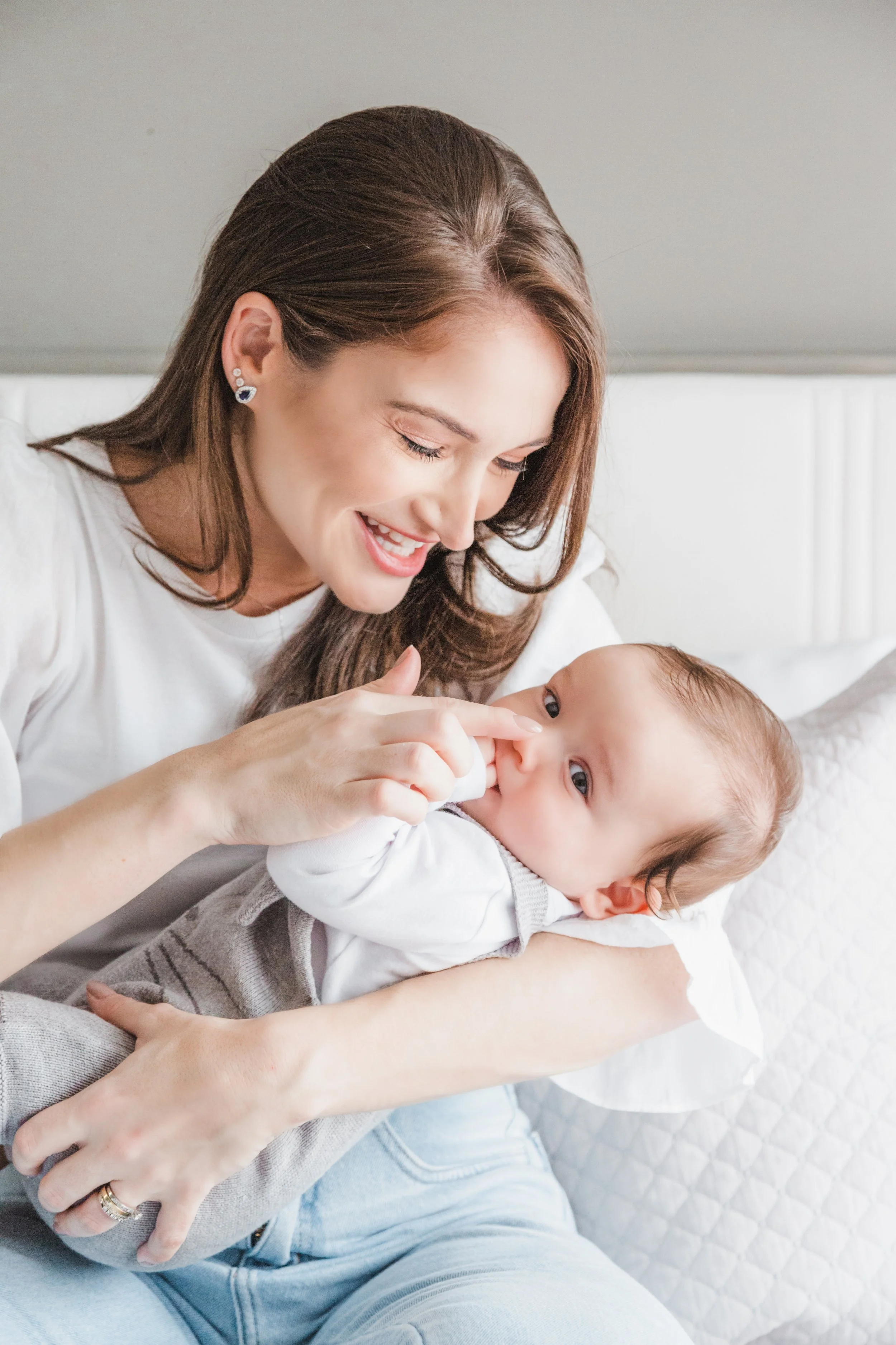 Mulher sorridente brincando com bebê deitado em seu colo, em ambiente claro e confortável.