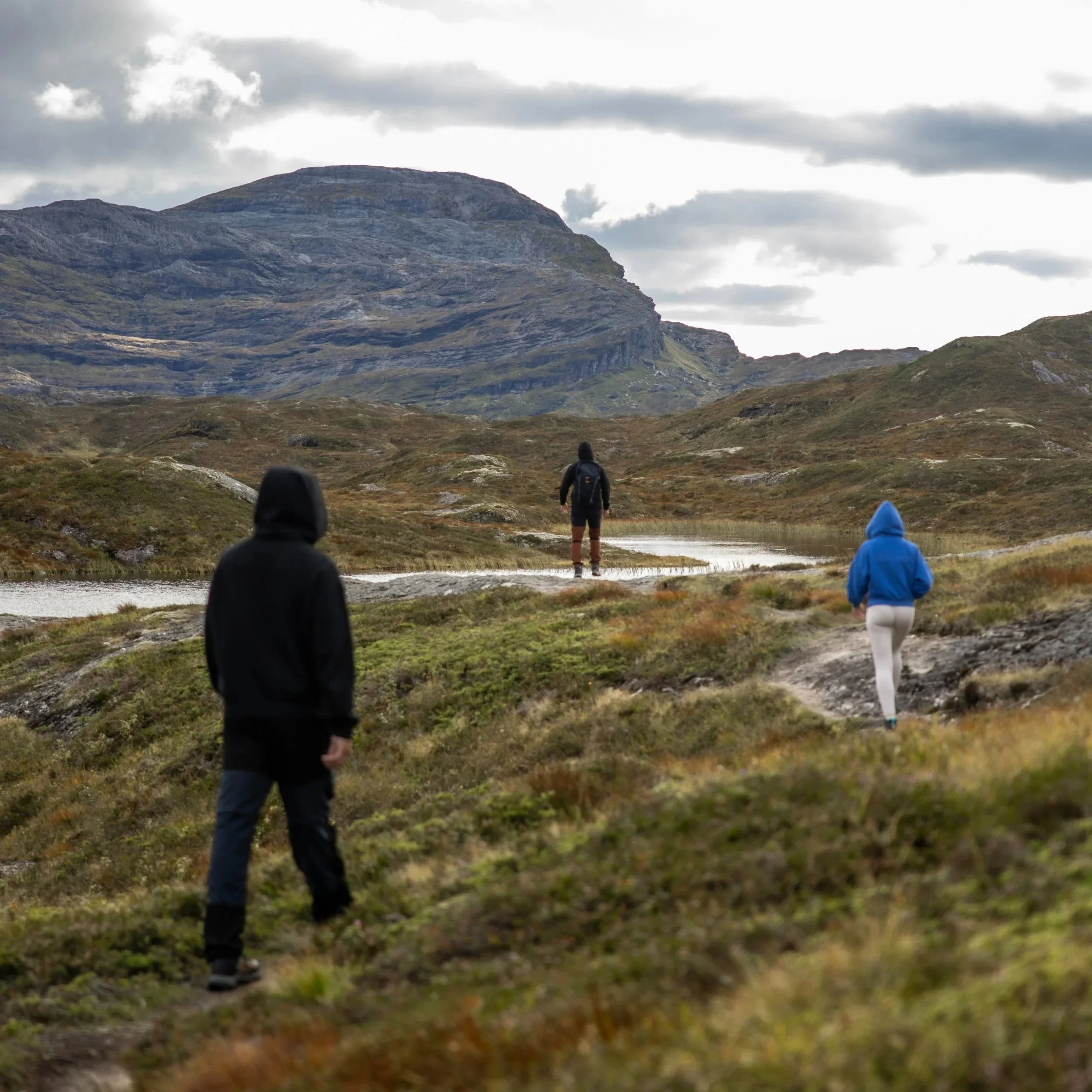 People hiking on a trail in a mountainous landscape with rocky hills and cloudy sky.