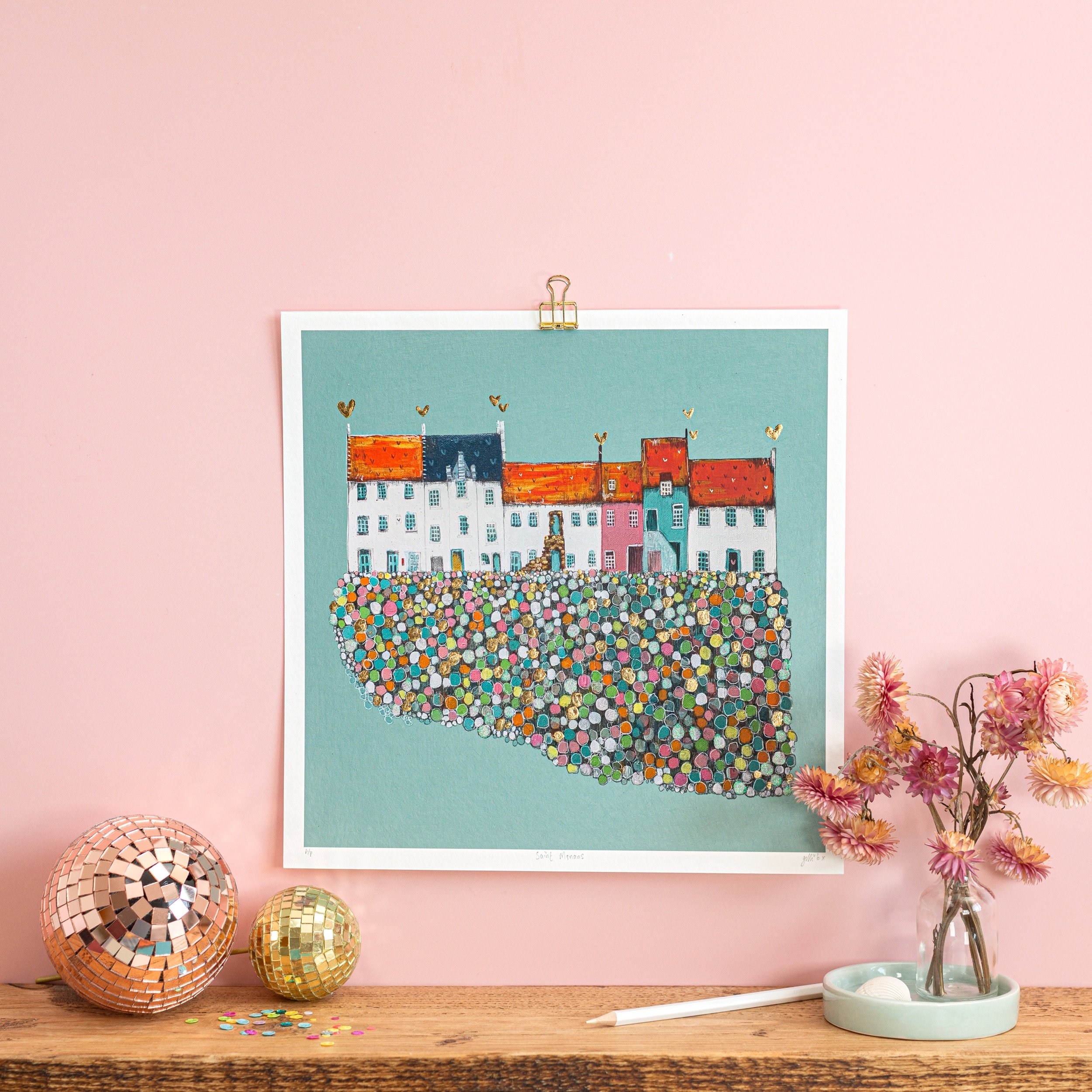 An East Neuk village illustration hangs on a pink wall above a shelf