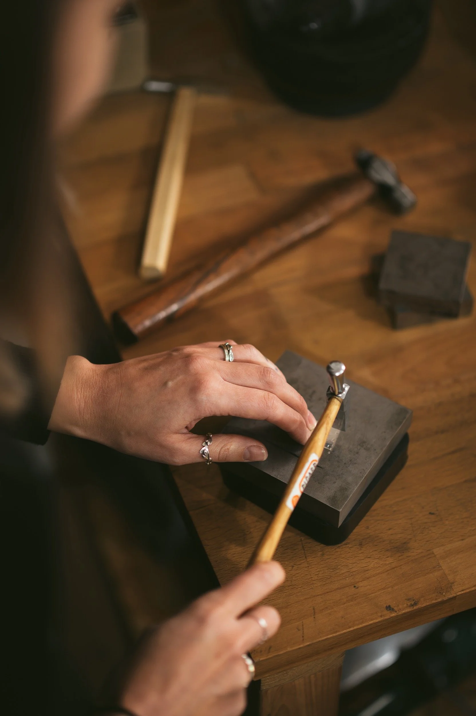 A person using a hammer and chisel on a piece of metal or stone, working on a workbench with various tools around.