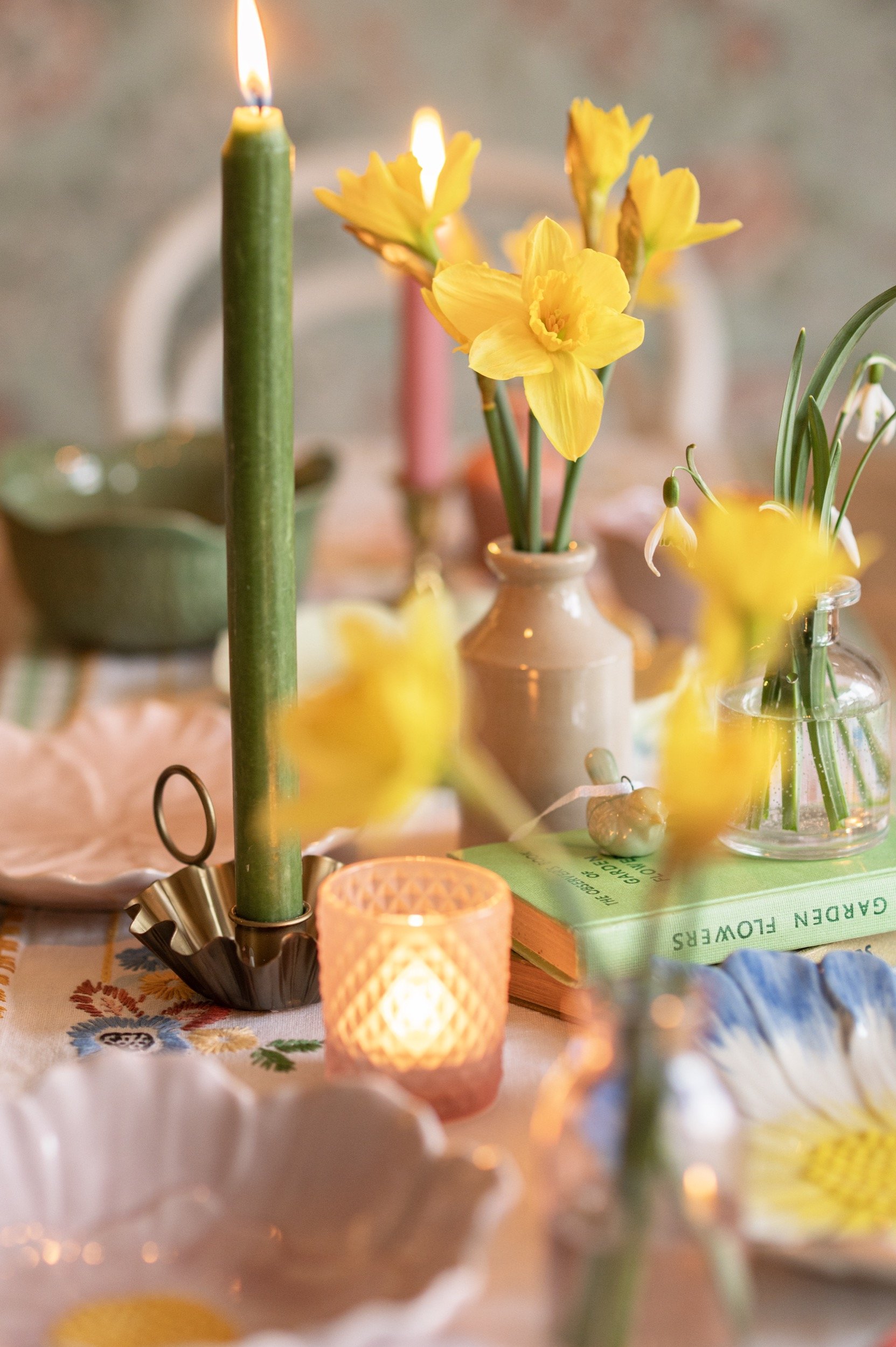 a table scene with candles and floral plates, along with vases of daffodils and snowdrops