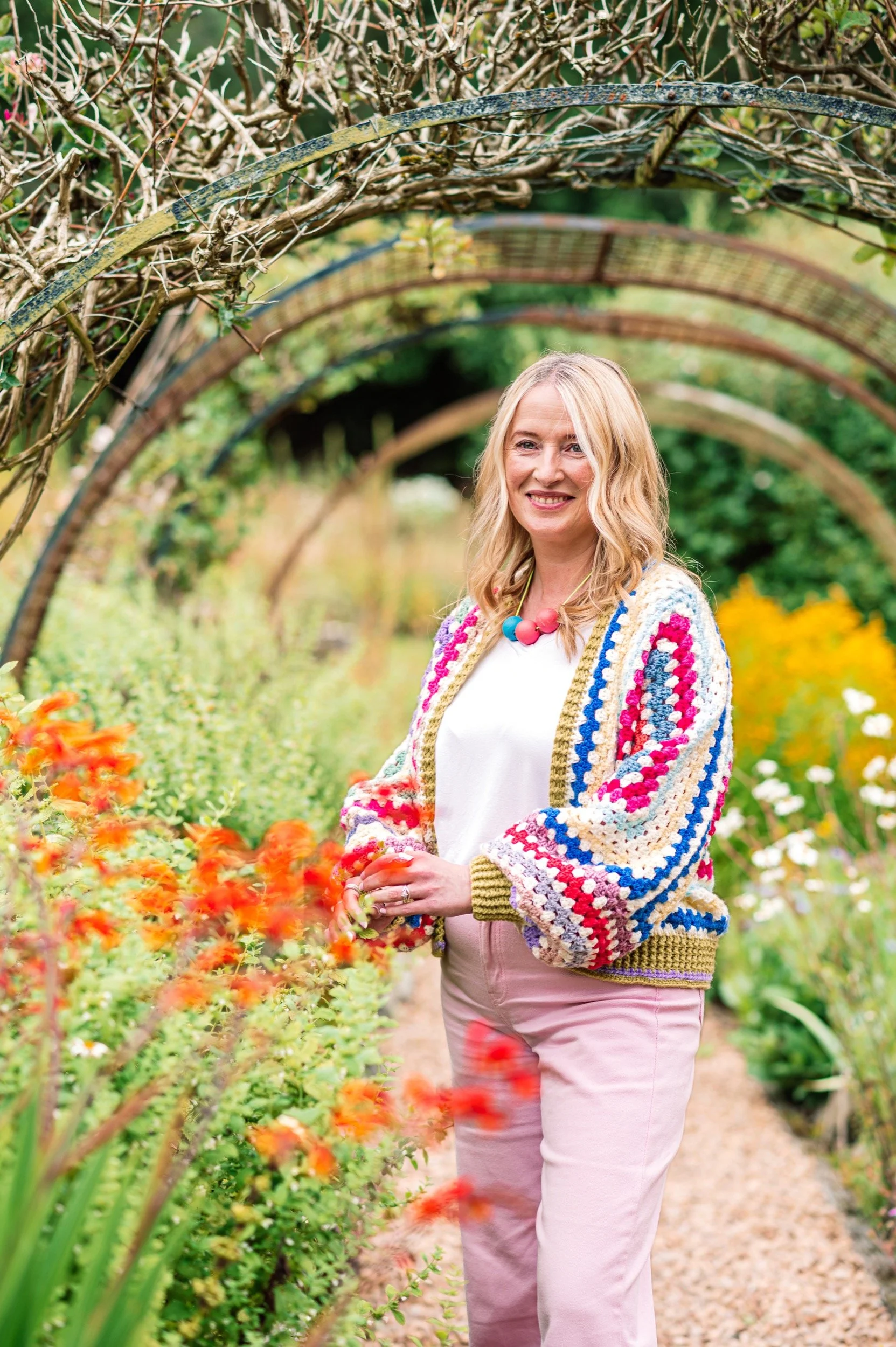 Melissa is standing in a wild flower garden, wearnig a colourful crochet cardigan