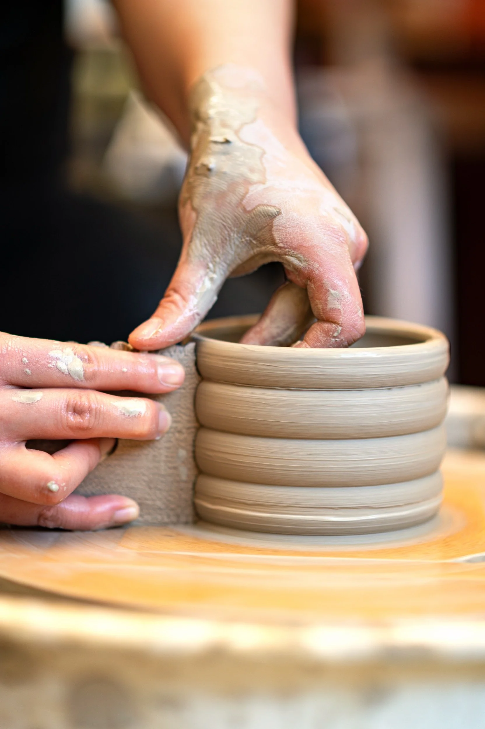 A person shaping a ceramic bowl on a pottery wheel, with their hands covered in clay.