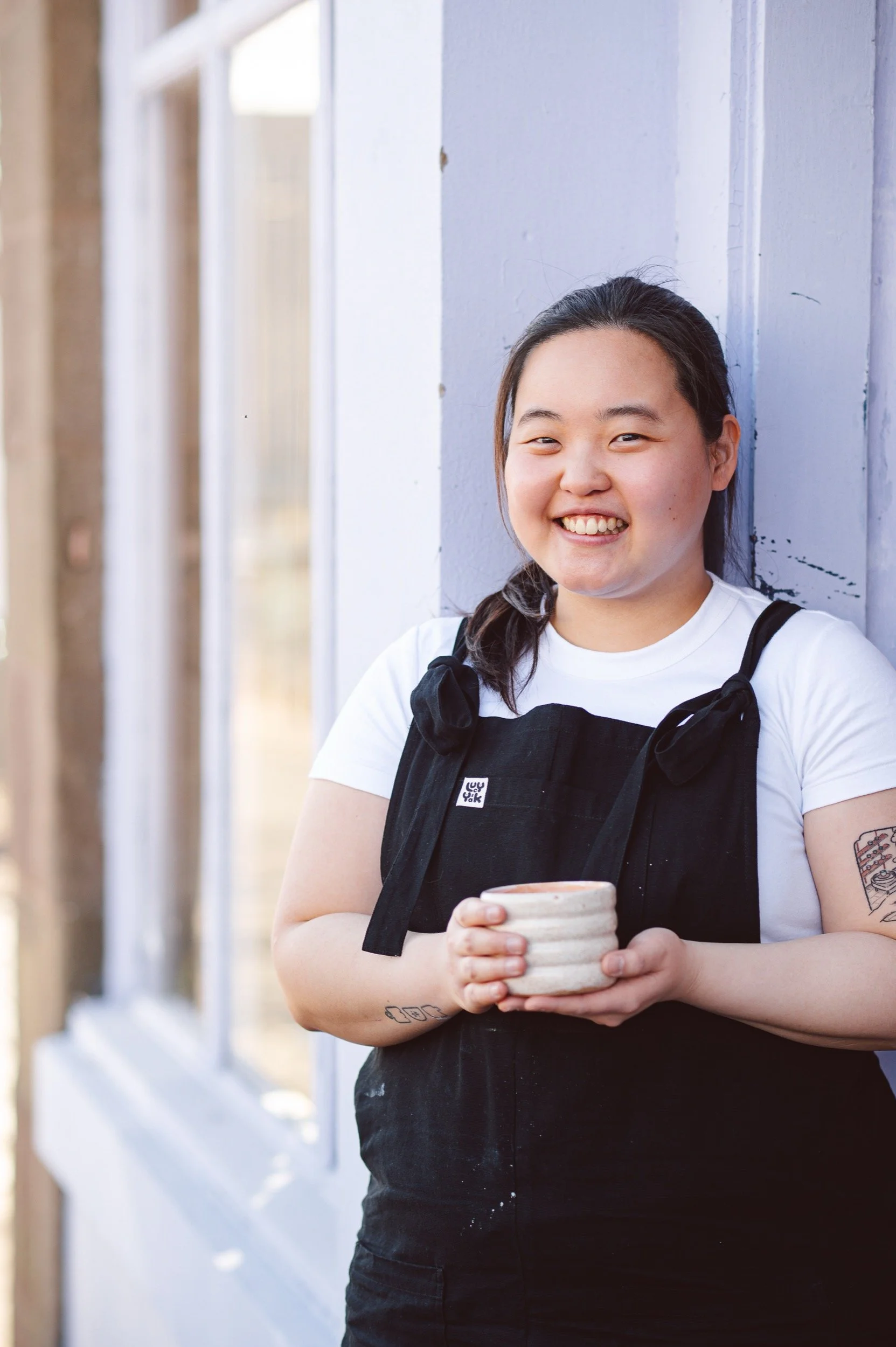 Wan Nee holds one of her ceramic cups outside a lilac coffee shop