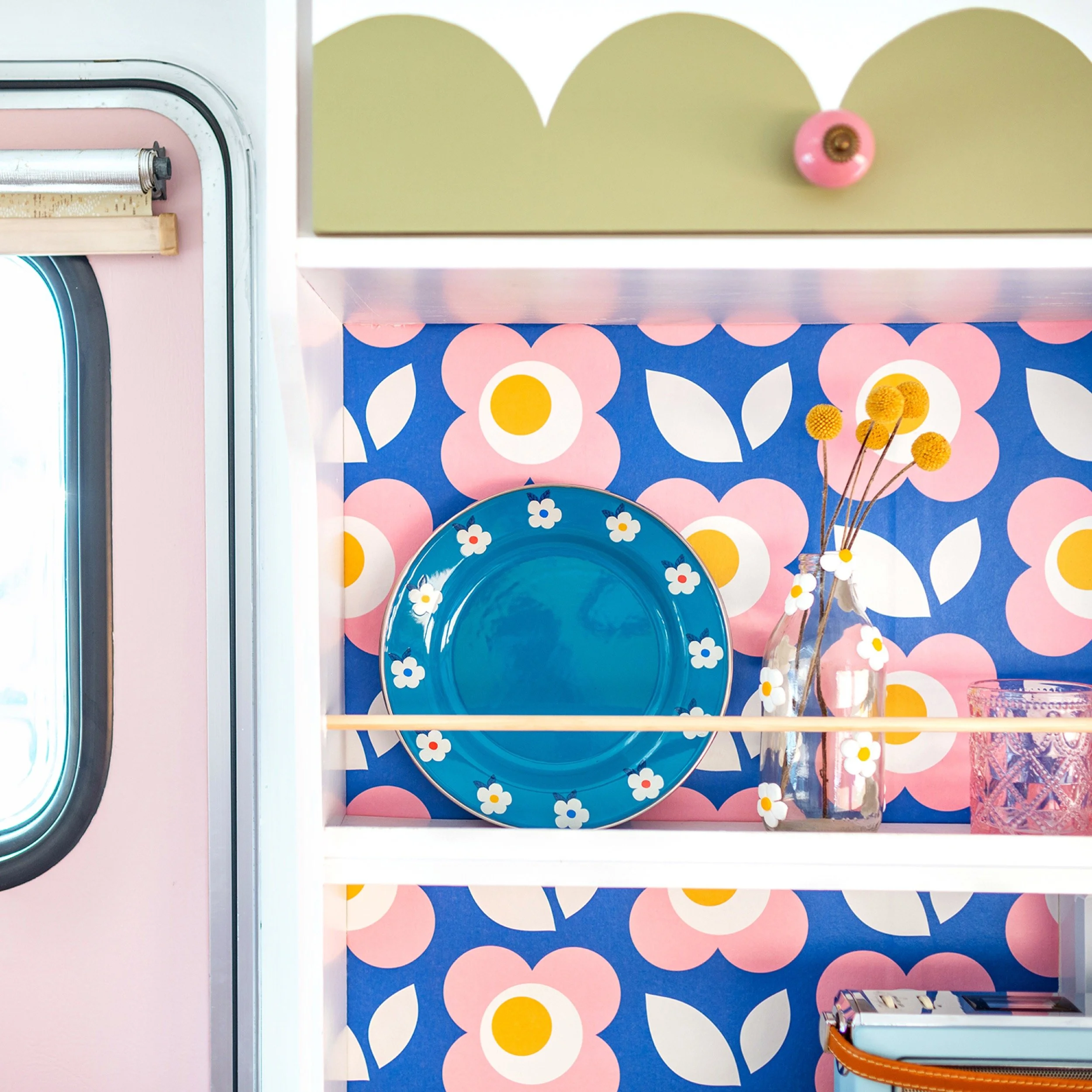 an enamel plate sits on the shelf of a vintage caravan with retro wallpaper