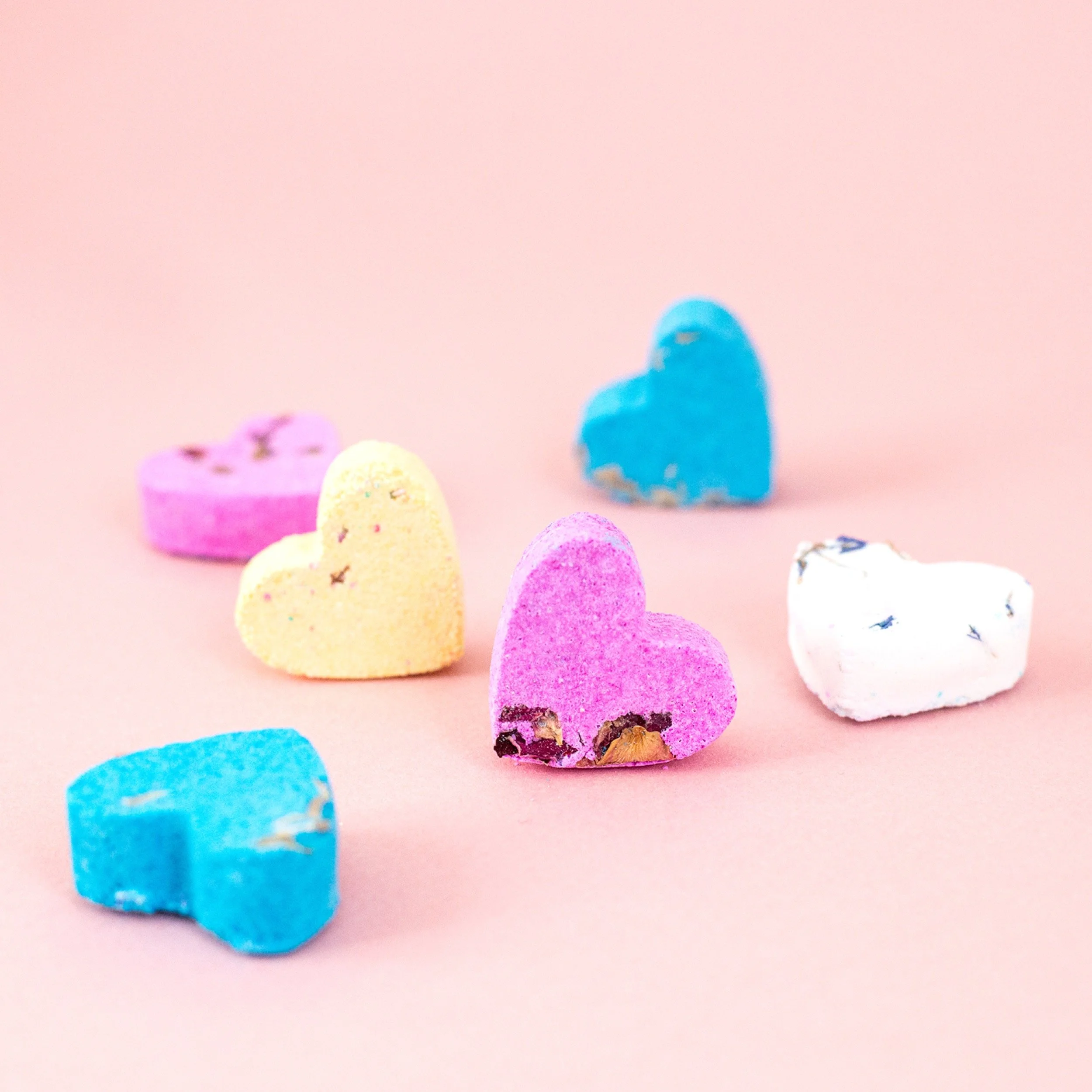 Colourful heart-shaped bath fizzers on a pink background.