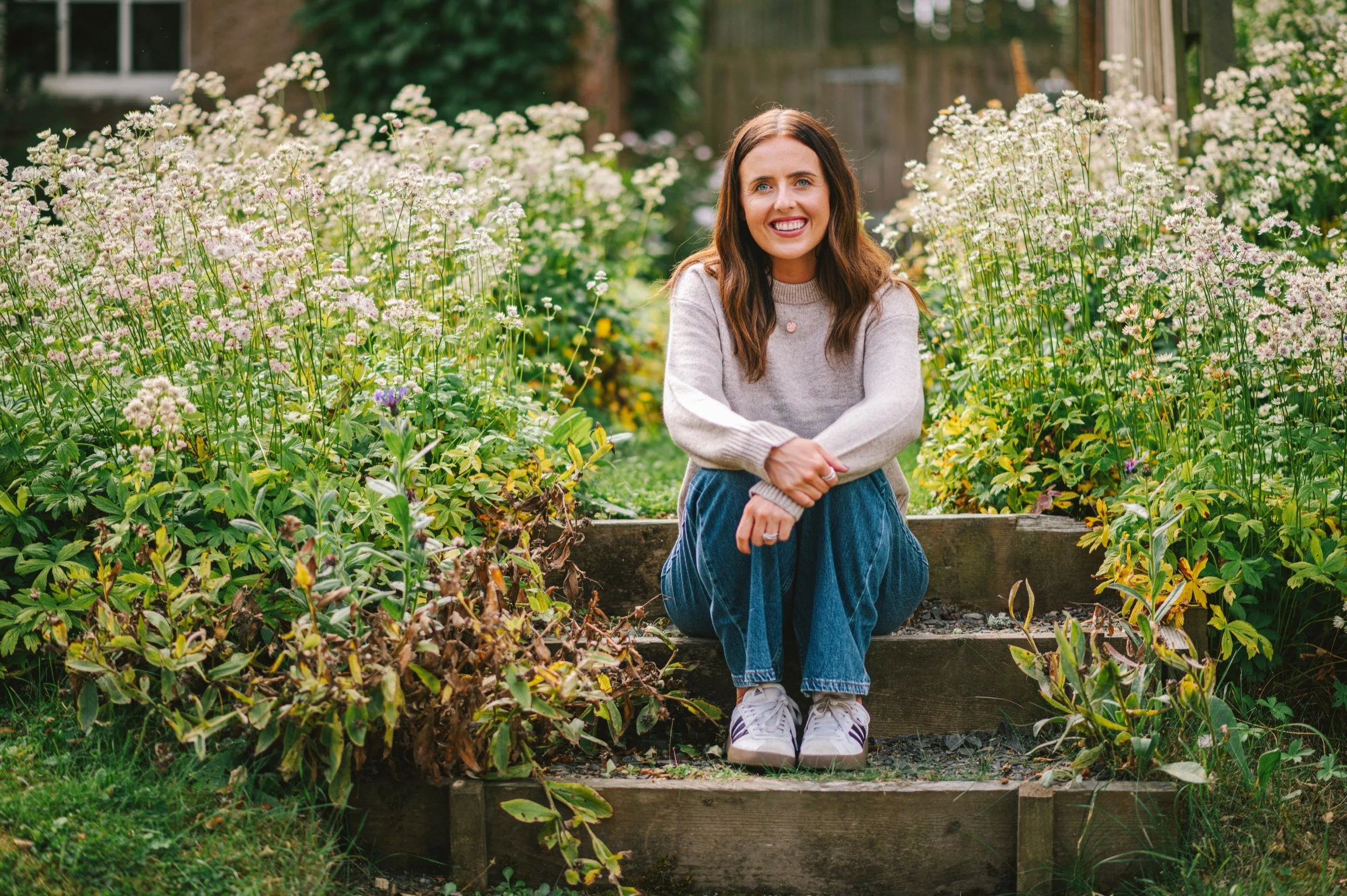 Lauren sits on steps between white wild flowers in a cottage garden
