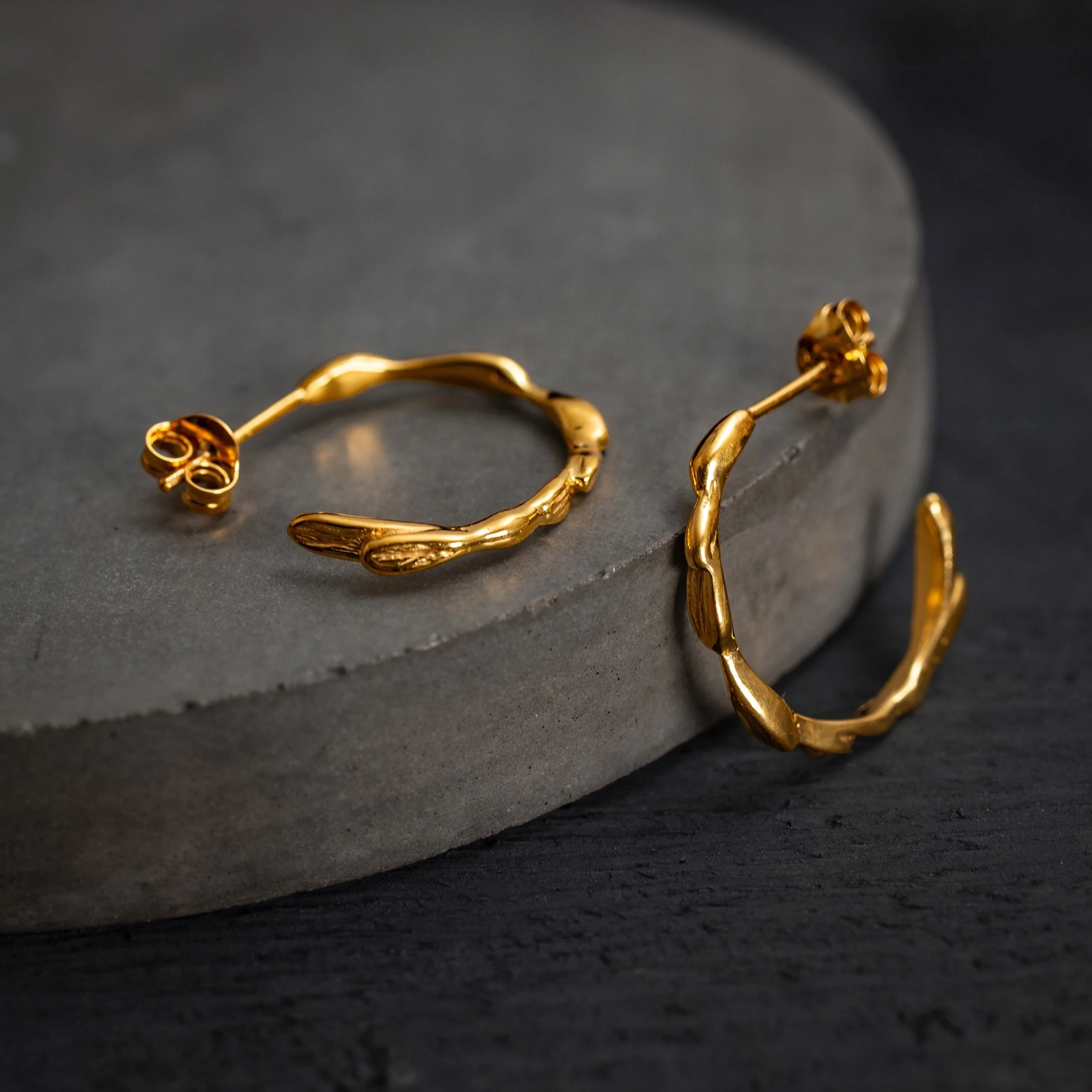 gold hoop earrings are photographed on a concrete coaster with charcoal wooden background