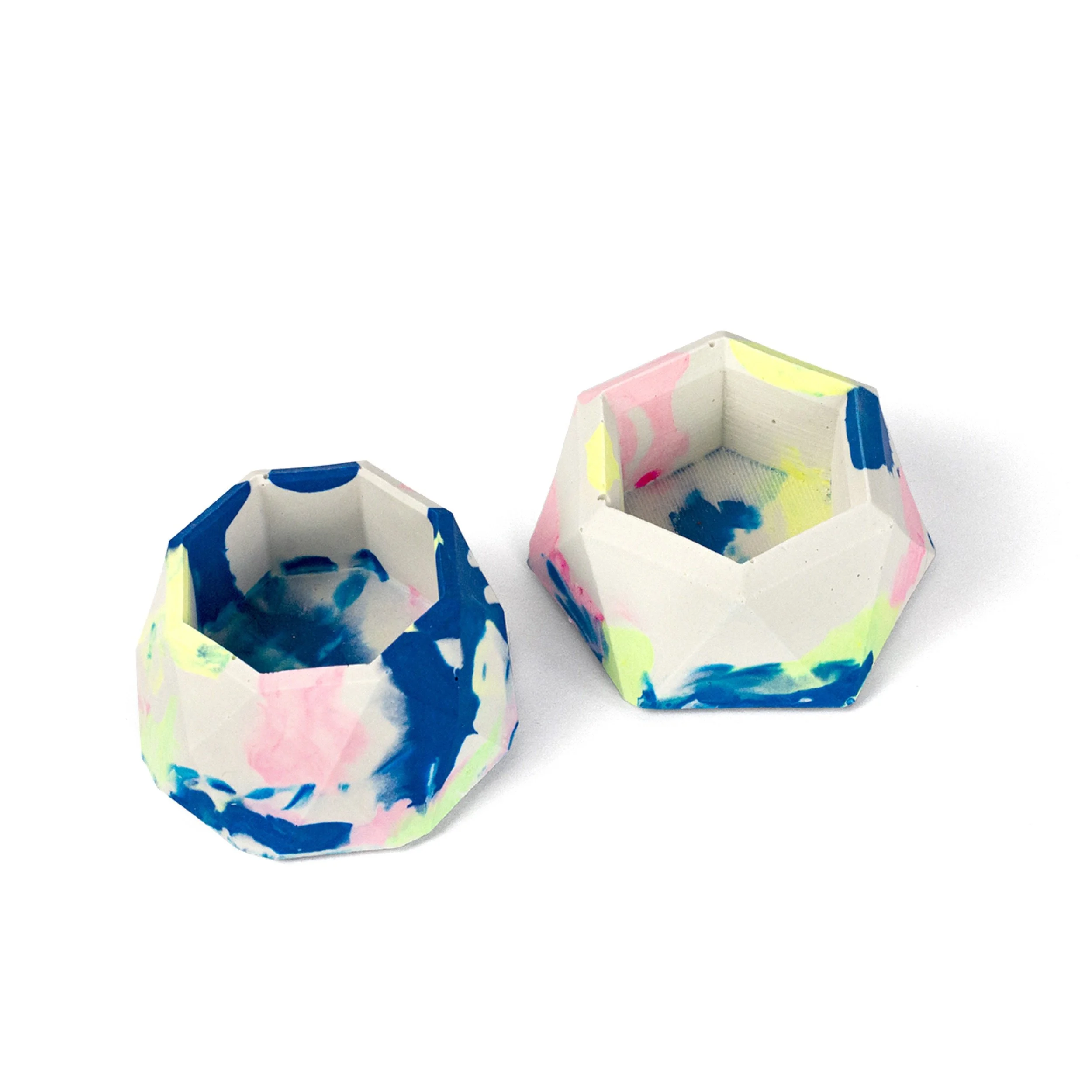 Two geometric, faceted containers with multicoloured jesmonite on a white background.