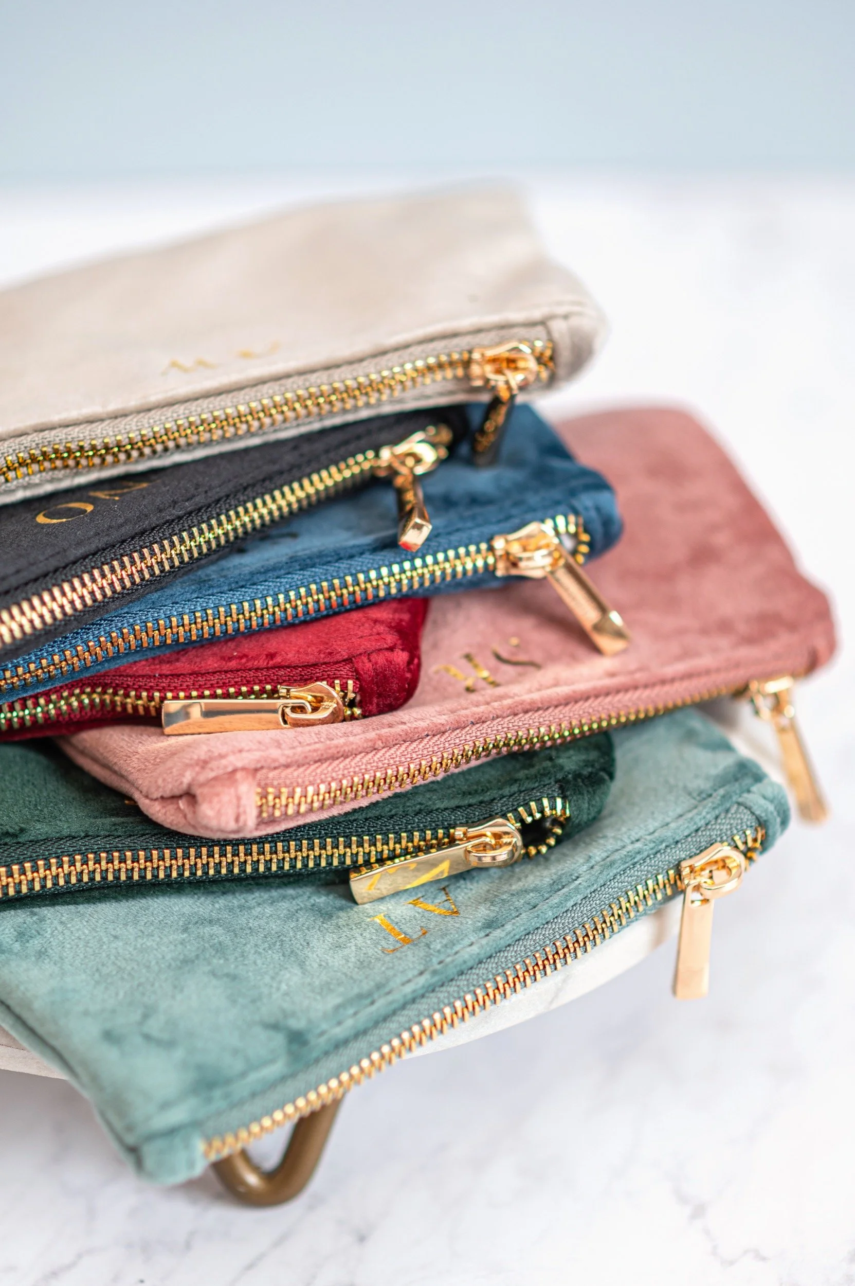 Colorful velvet pouches with gold zippers stacked on a white surface.