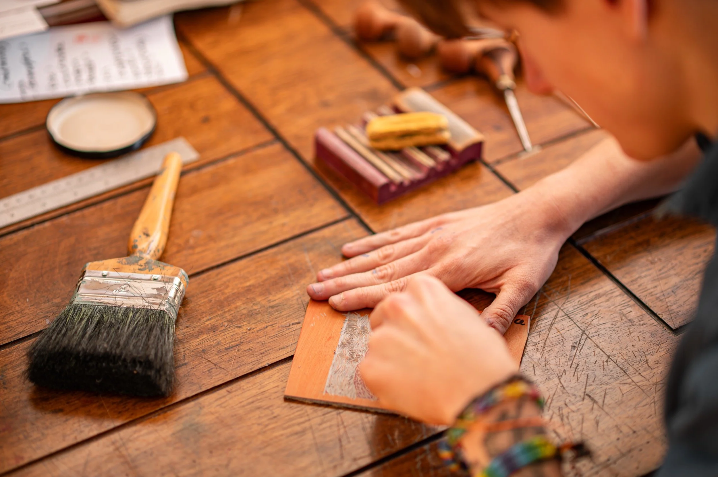 Person carving a lino cutting, with painting tools and brushes on the table.