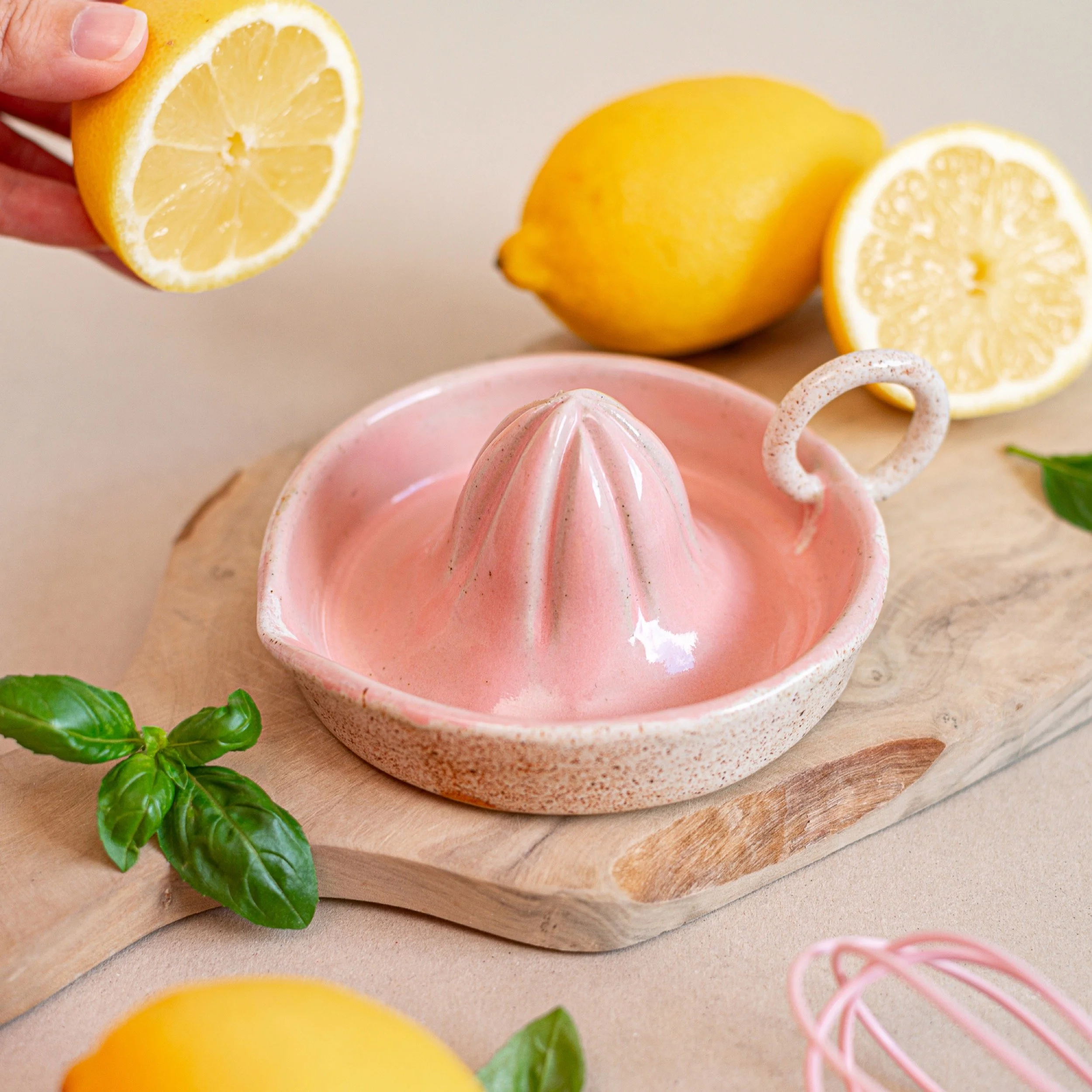 a pink lemon juicer sits on a wooden chopping board with lemons