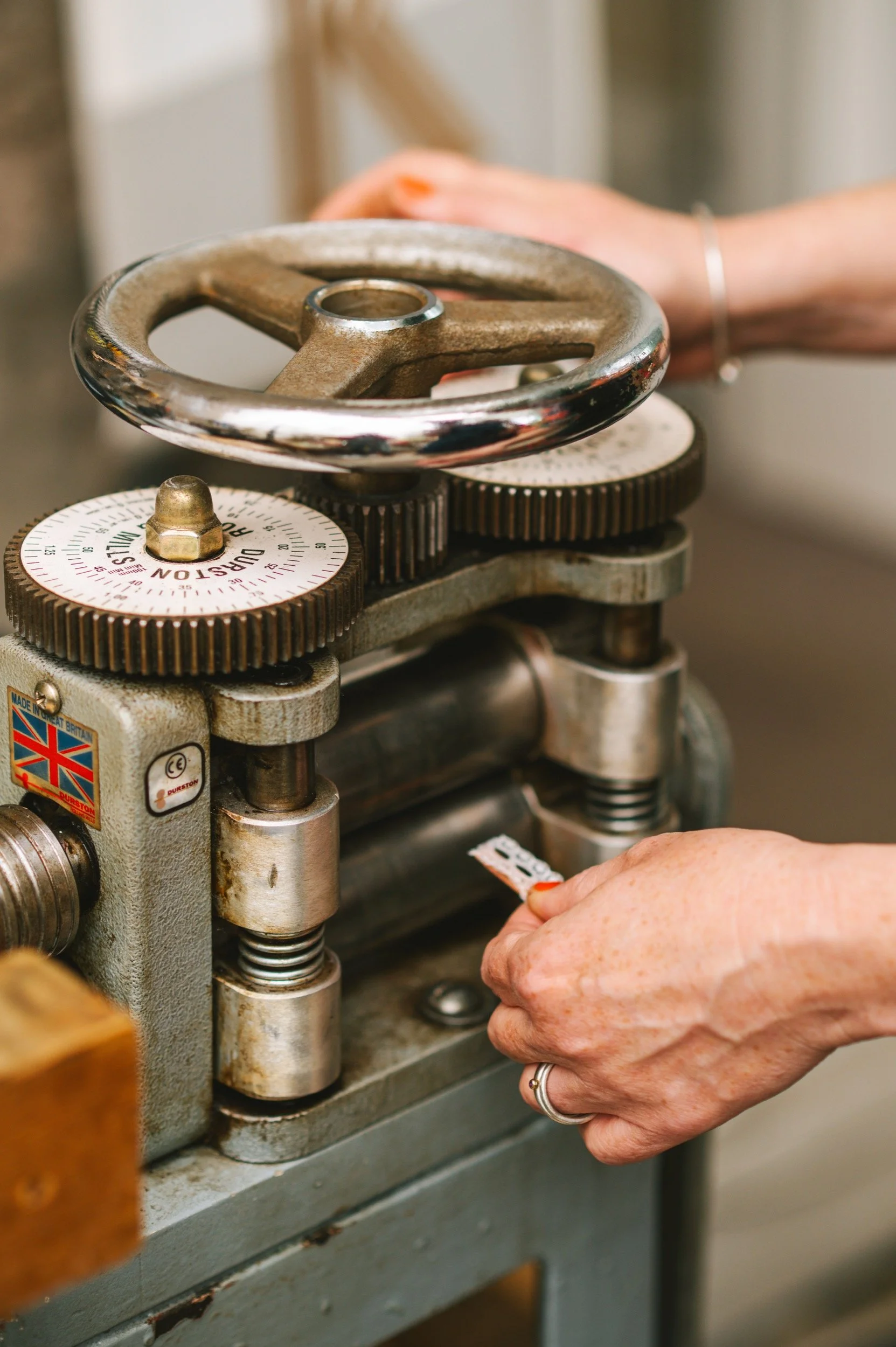Close-up of a vintage metal machine with a large wheel and gears, being operated by a person's hands.