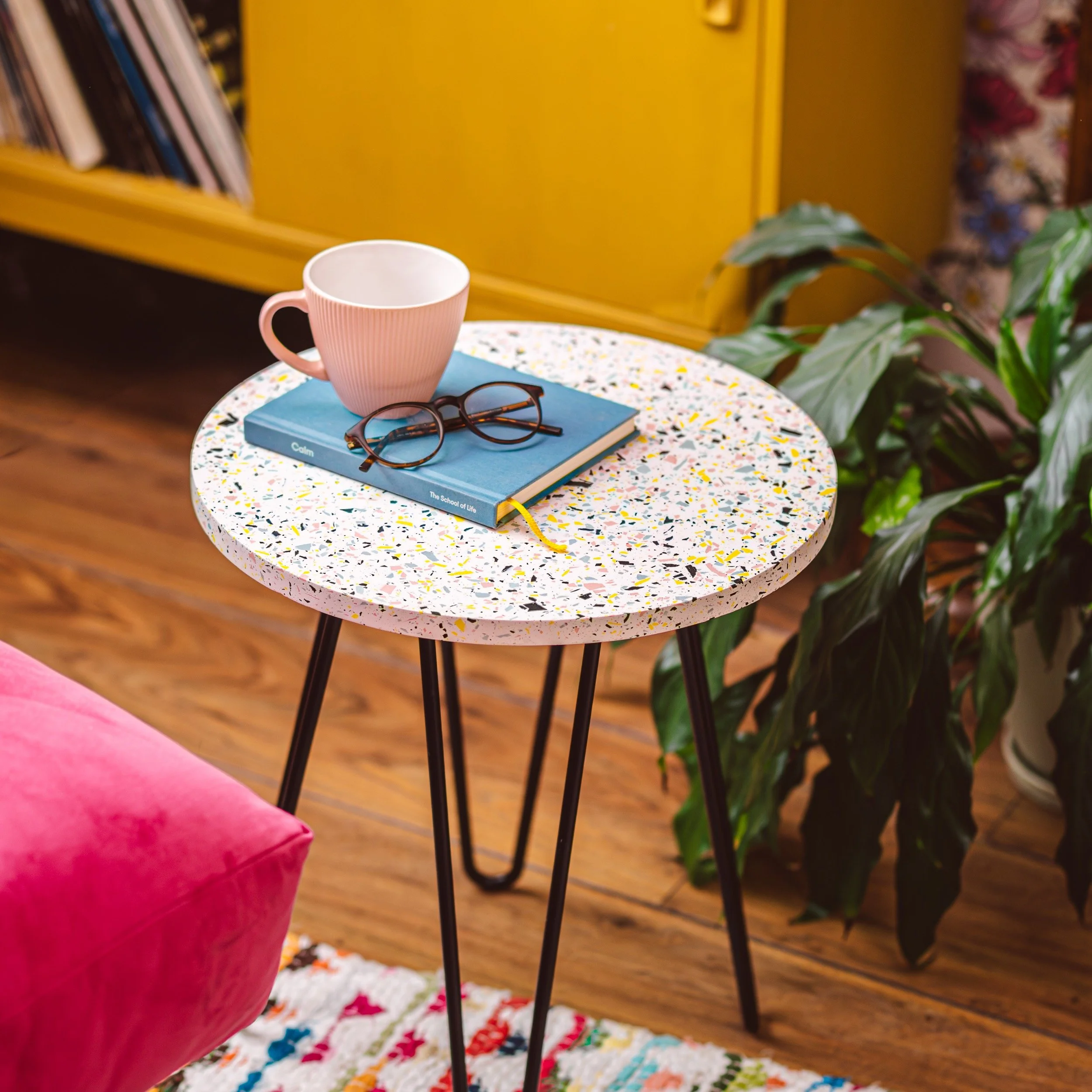 a terrazzo side table sits in a living room with sideboard and plant behind