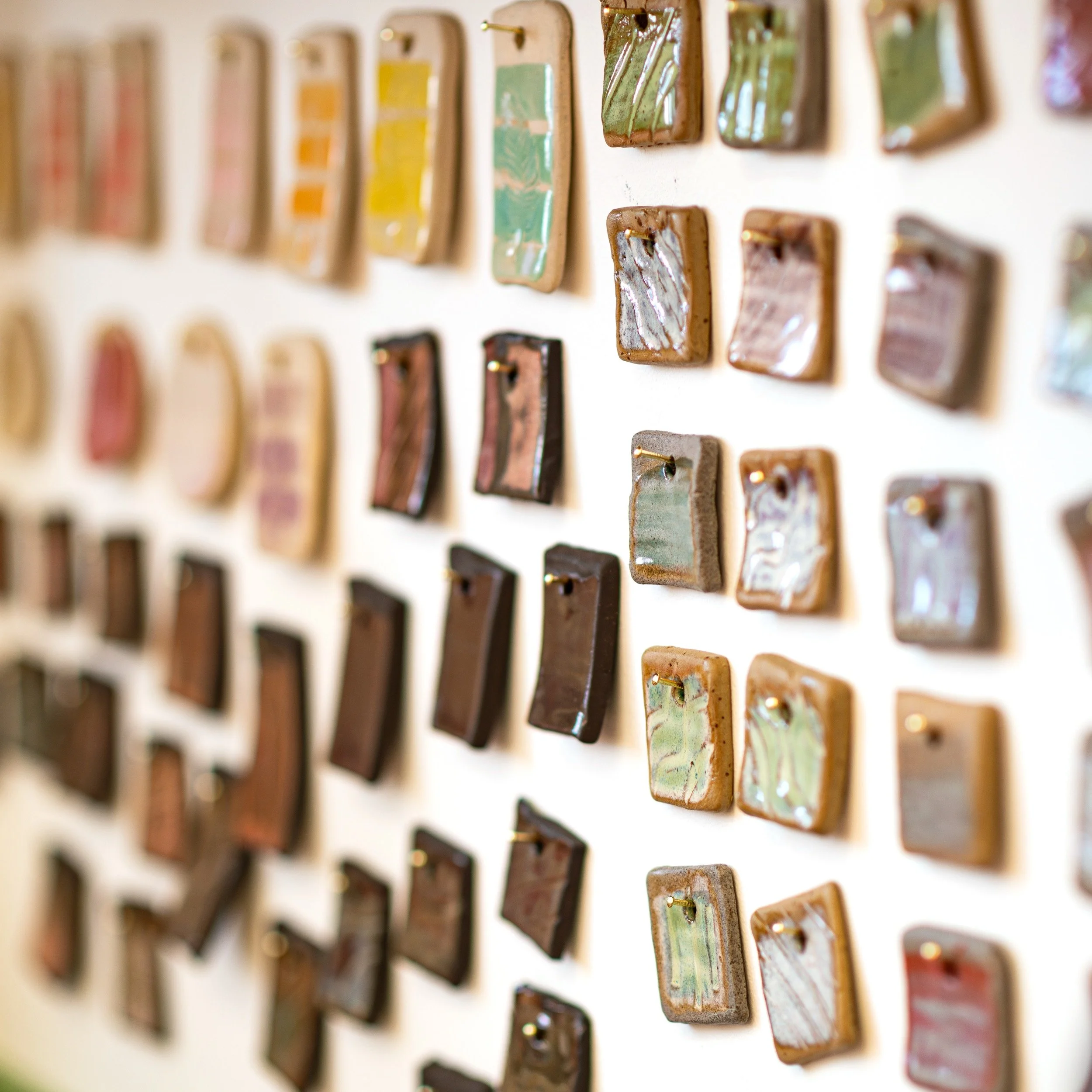 Display of colourful glazed ceramic tiles arranged on a white wall.