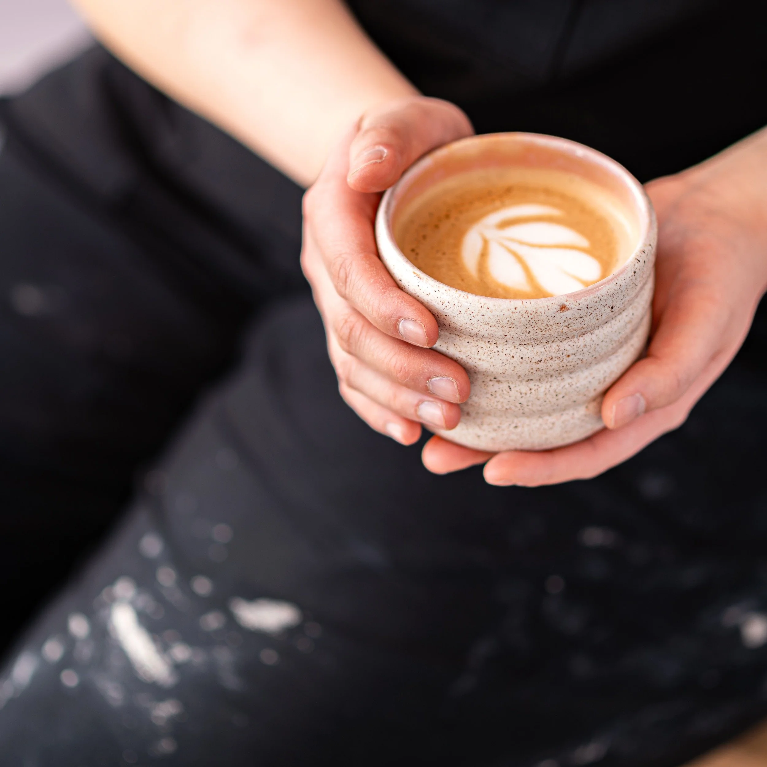 Person holding a ceramic cup of latte with latte art in their hands.
