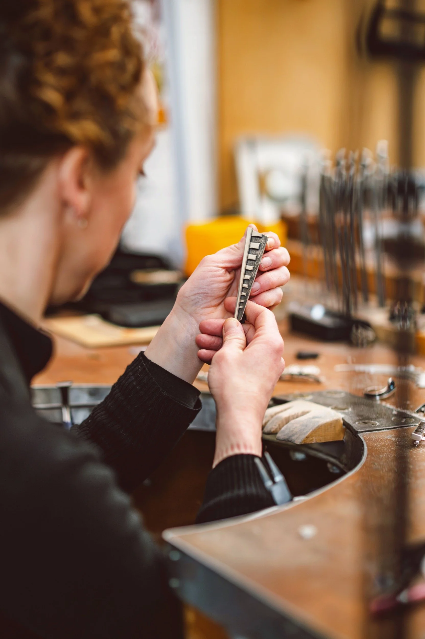 A woman admiring her silver work, surrounded by various small tools and items on a wooden table.