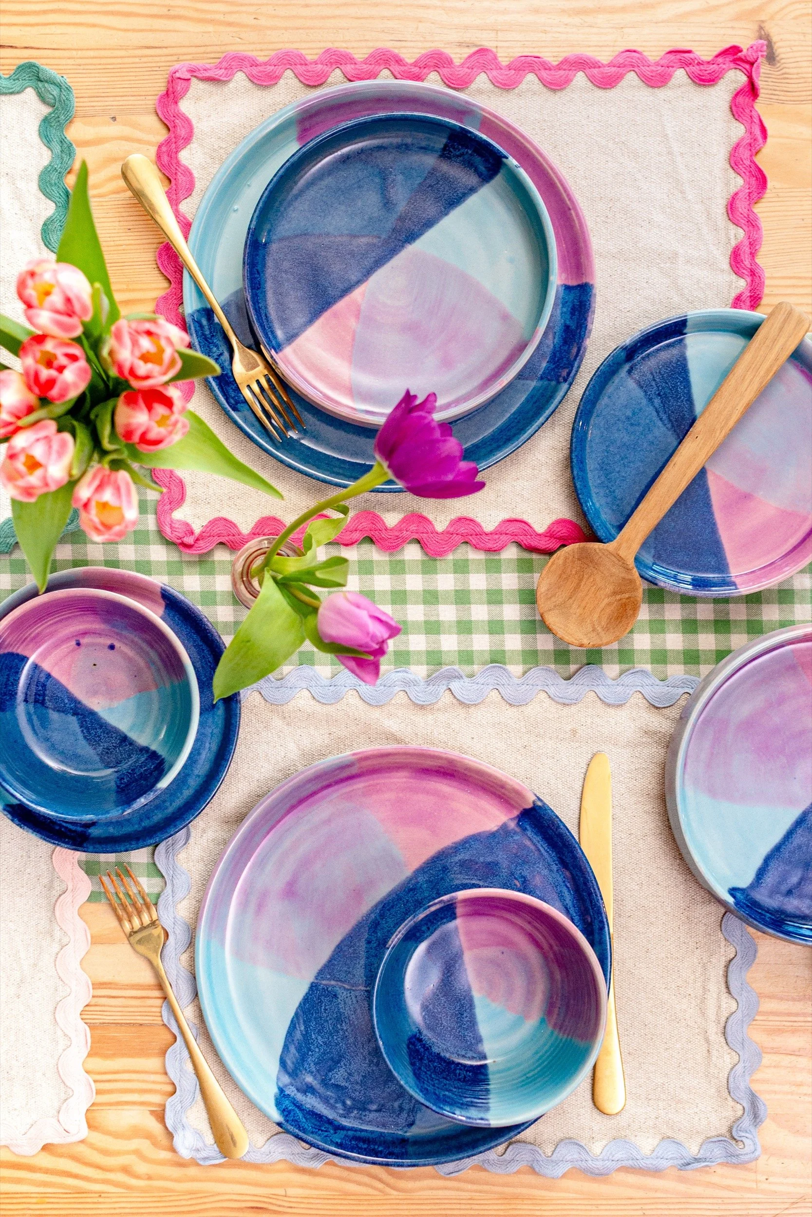 a flatlay of ceramic dinnerware with colourful table linen and tulips