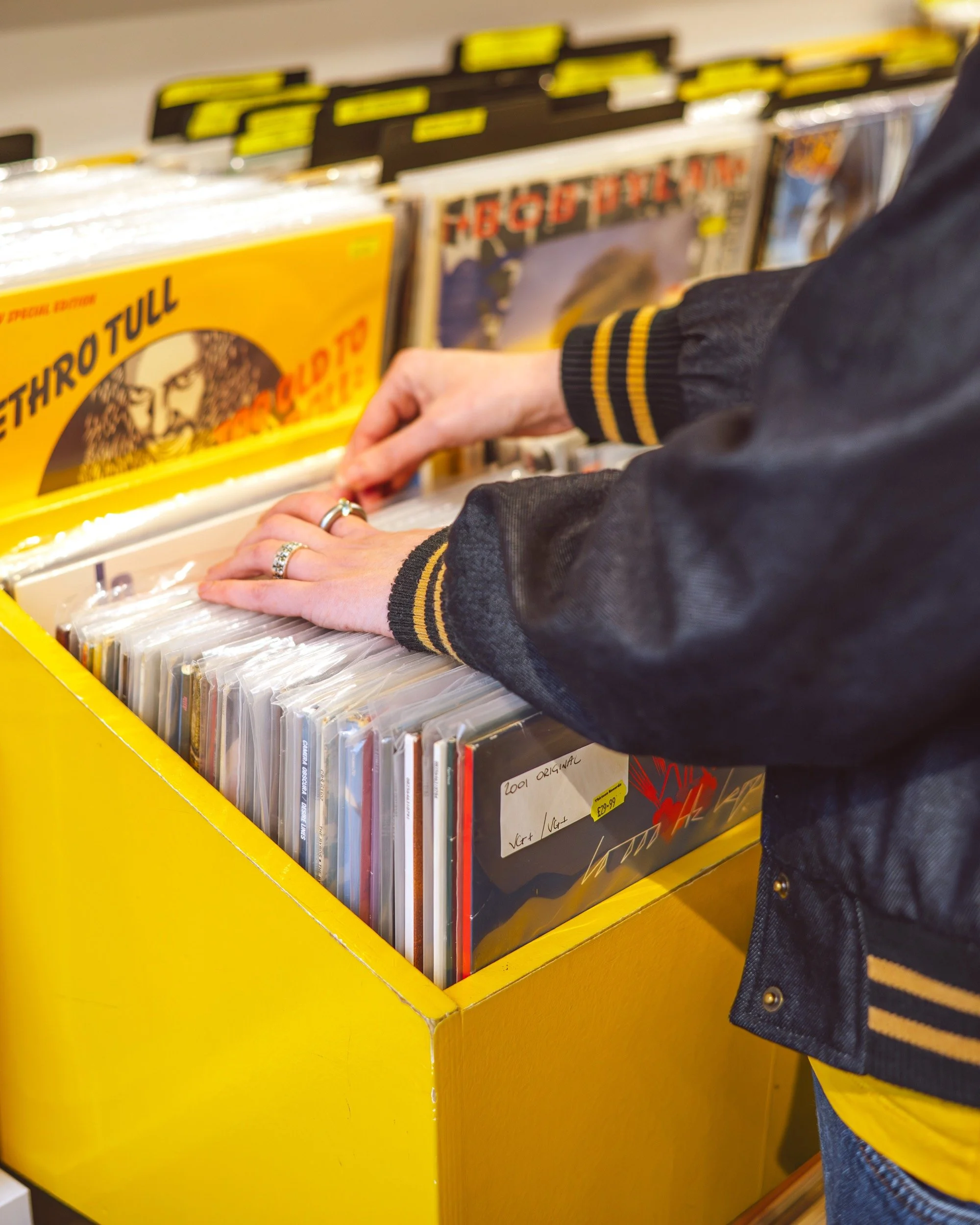 Person browsing through vinyl records in a yellow bin at a record store.