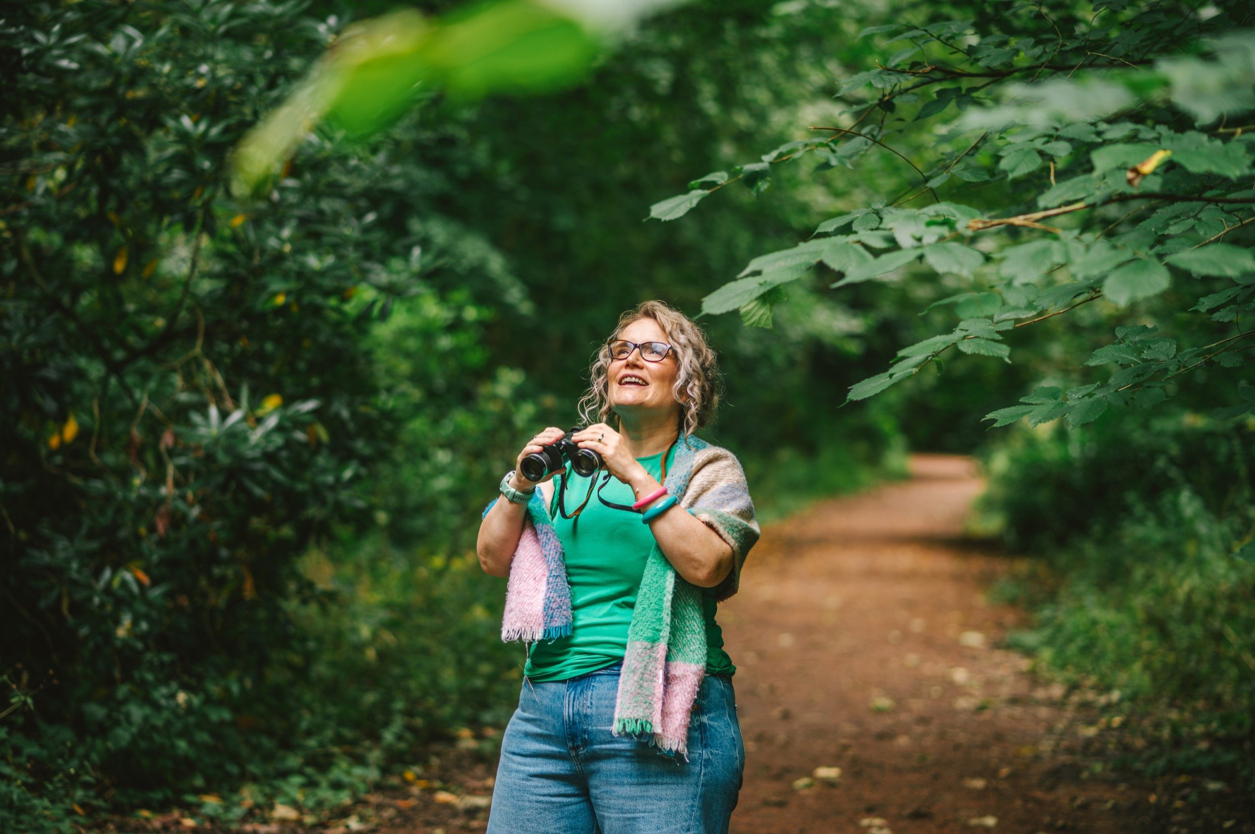 Jenna stands with binoculars in the forest