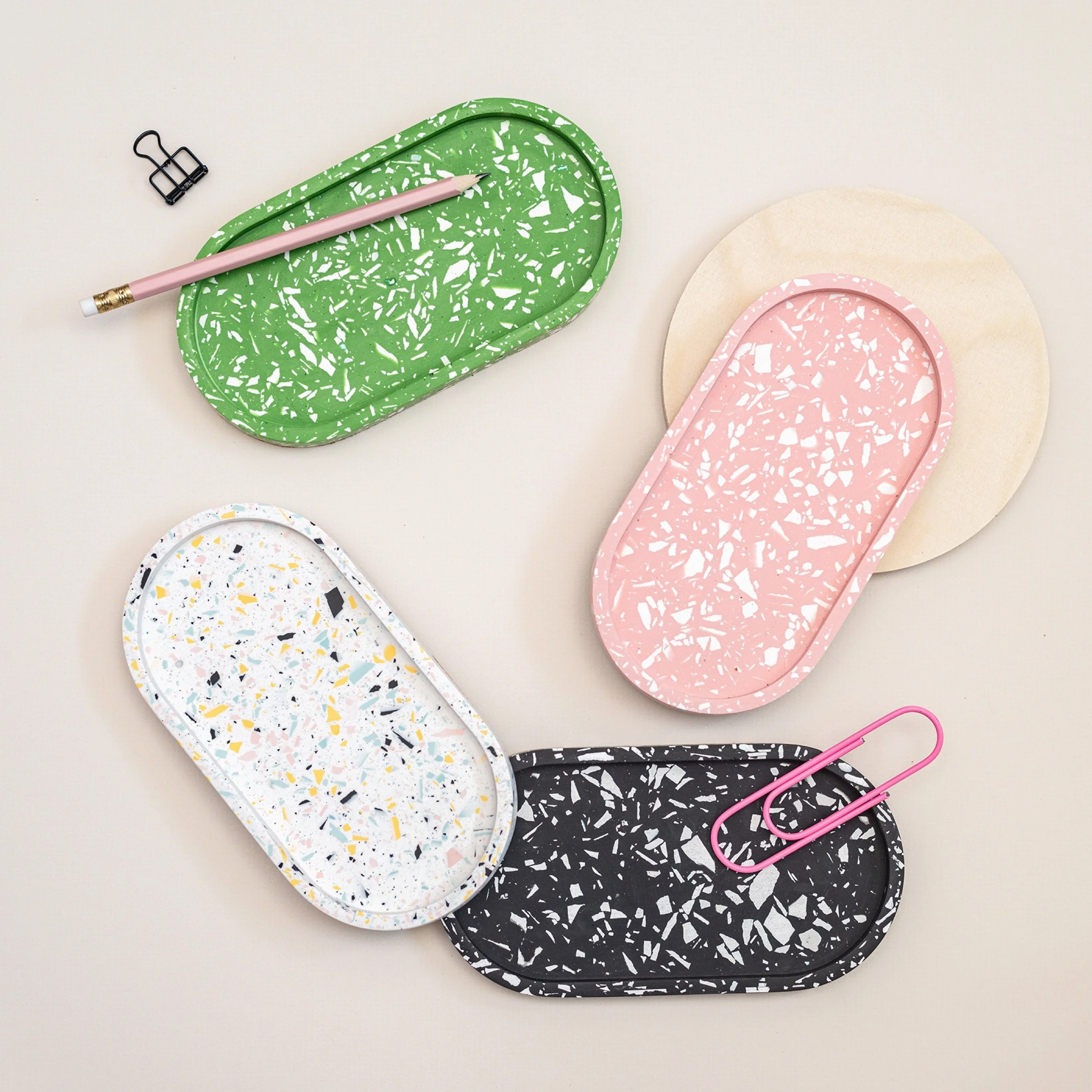 Colorful terrazzo-patterned trays and accessories including a pink paperclip, a pink pencil, and a black binder clip on a white surface.