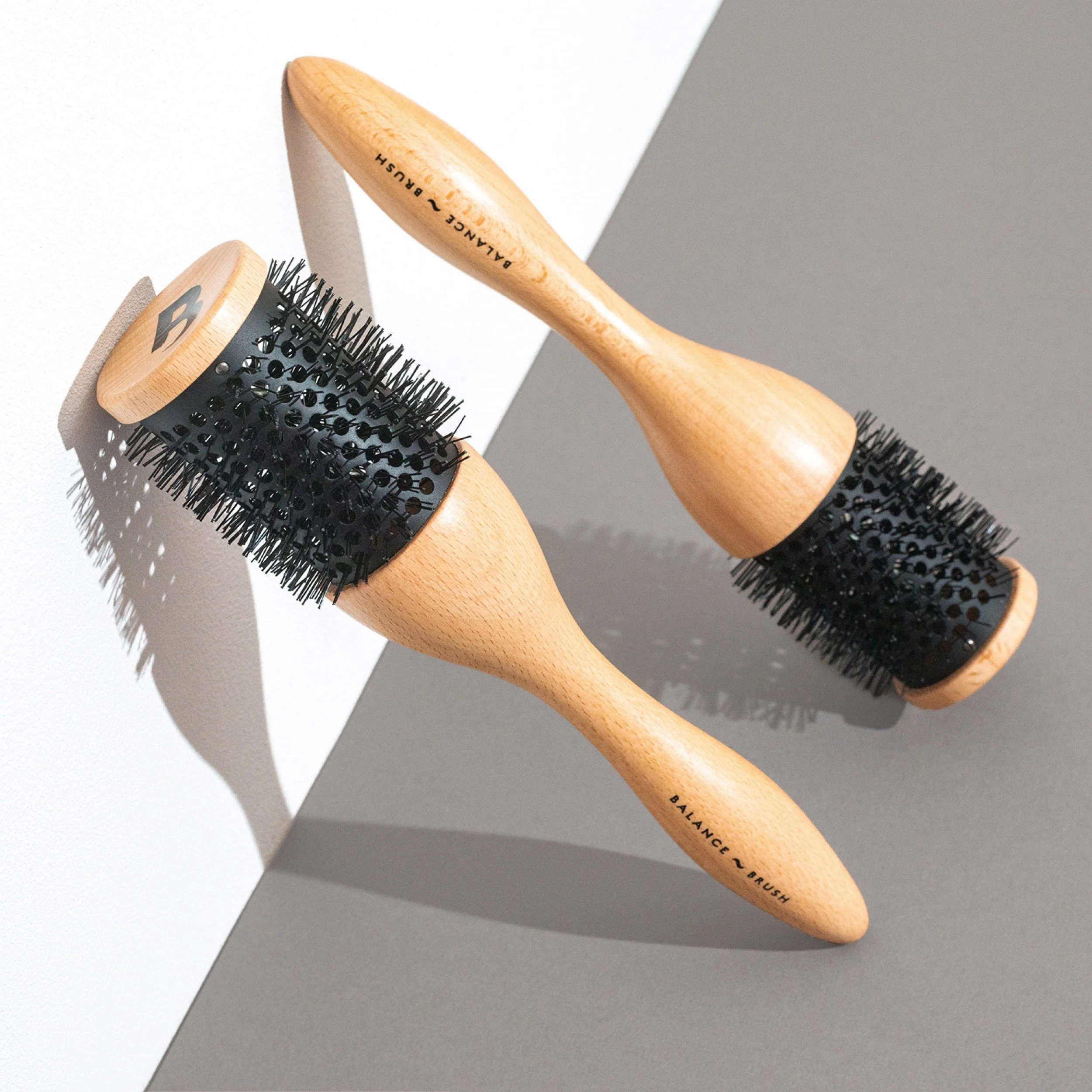 Two wooden hairbrushes with black bristles placed on a gray and white surface.