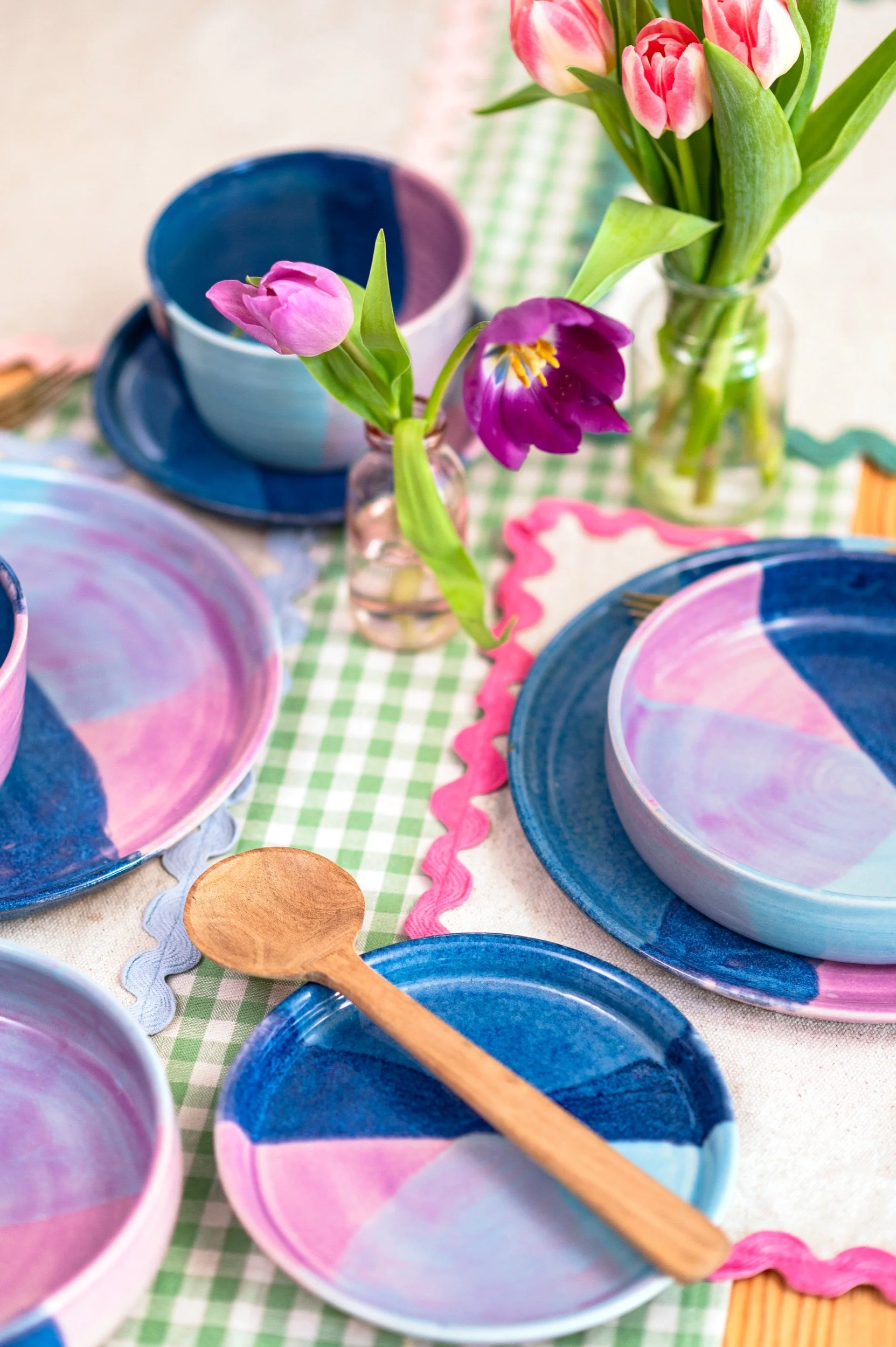 pink and blue ceramic dinnerware is photographed on a dining table with flowers