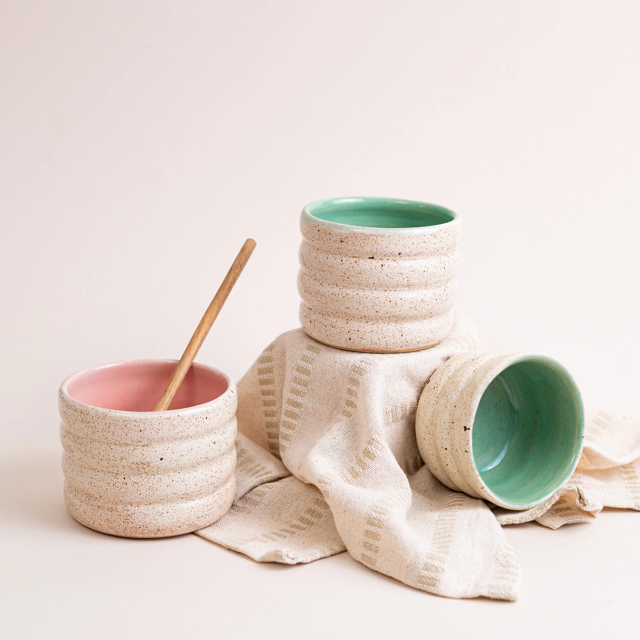 Three ceramic bubble tumblers are photographed with minimal styling, a neutral linen and wooden spoon.