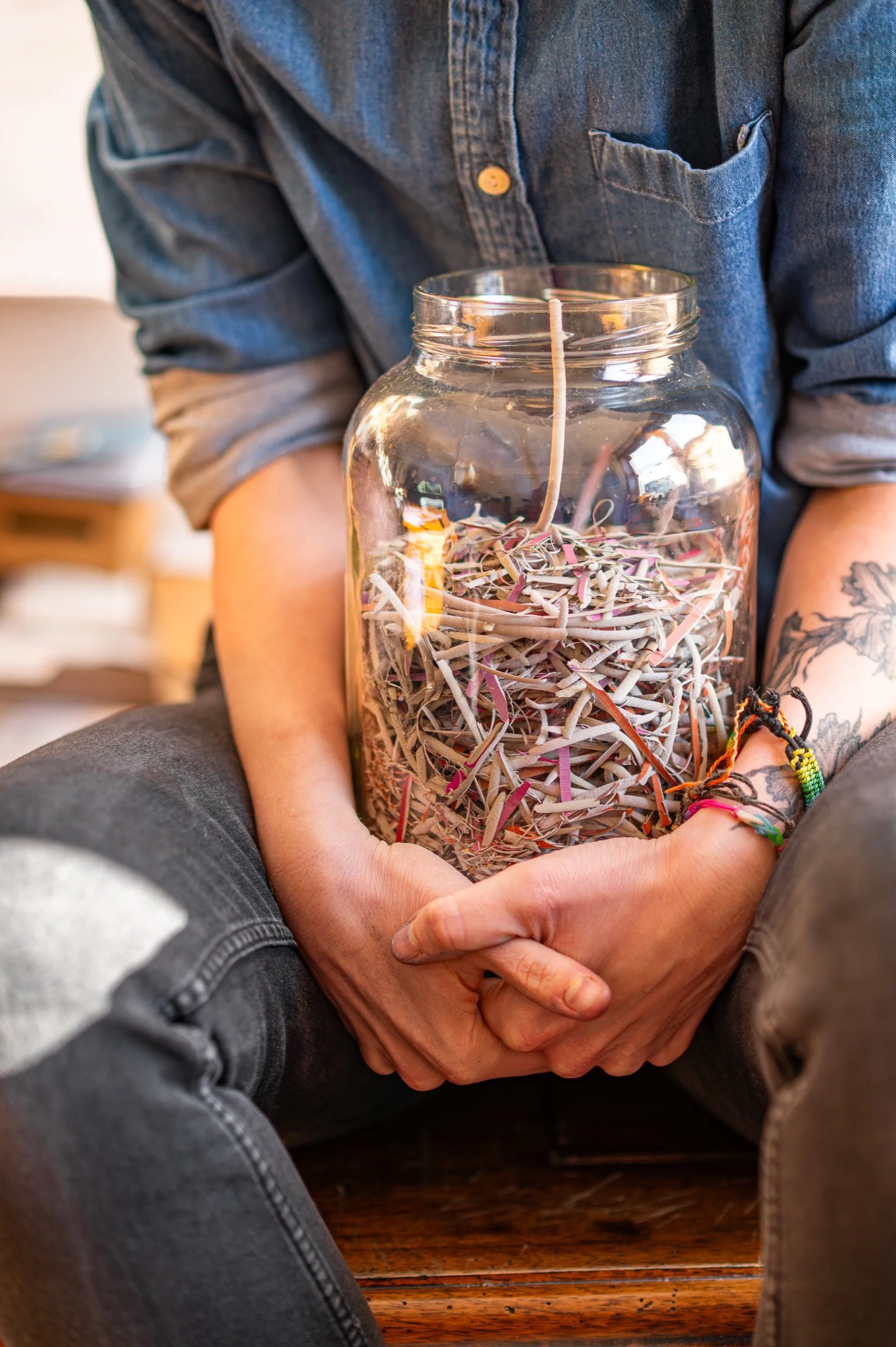 Person sitting cross-legged, holding a glass jar filled with lino off-cuts