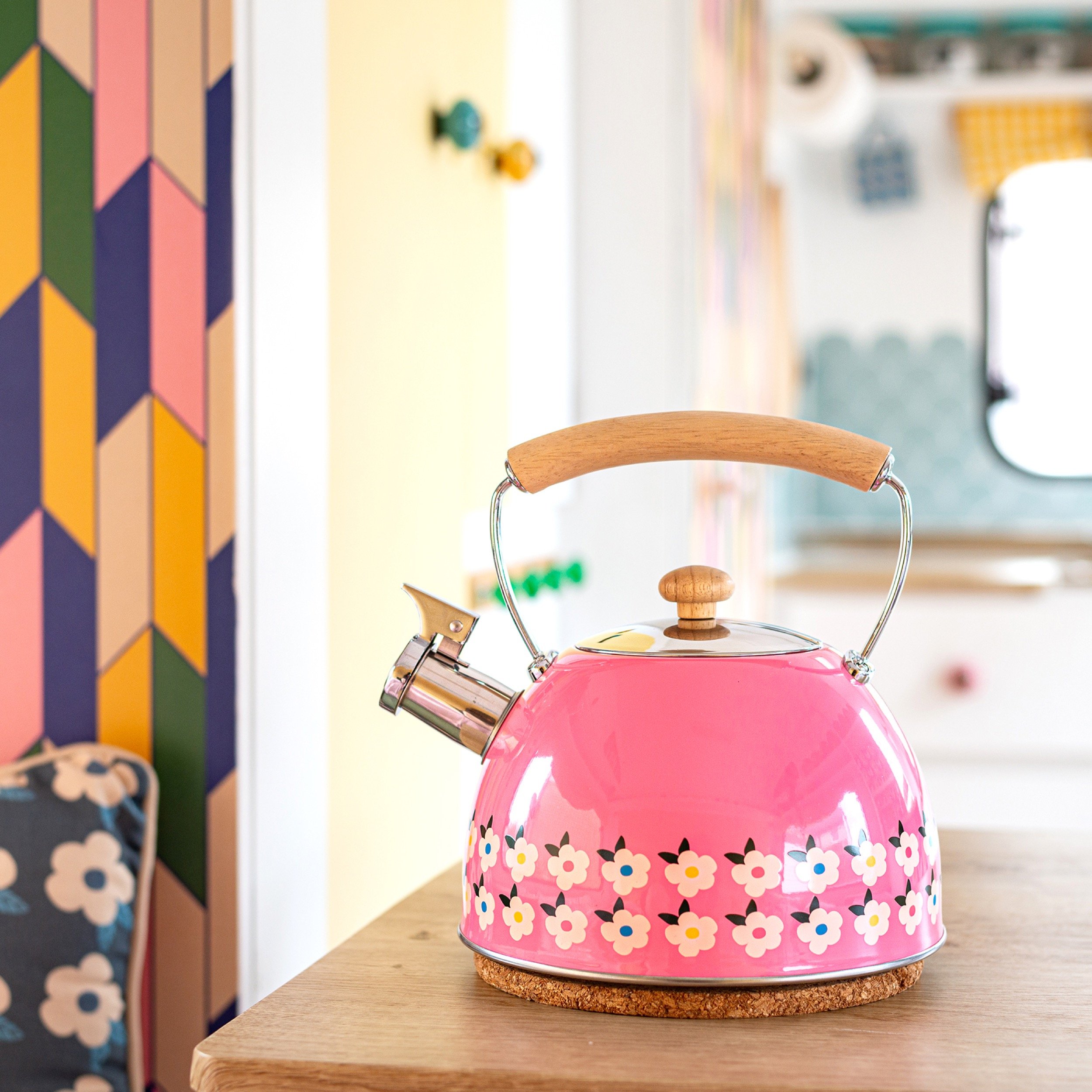 Pink vintage kettle with floral pattern on a wooden table in a colorful, retro-style interior.