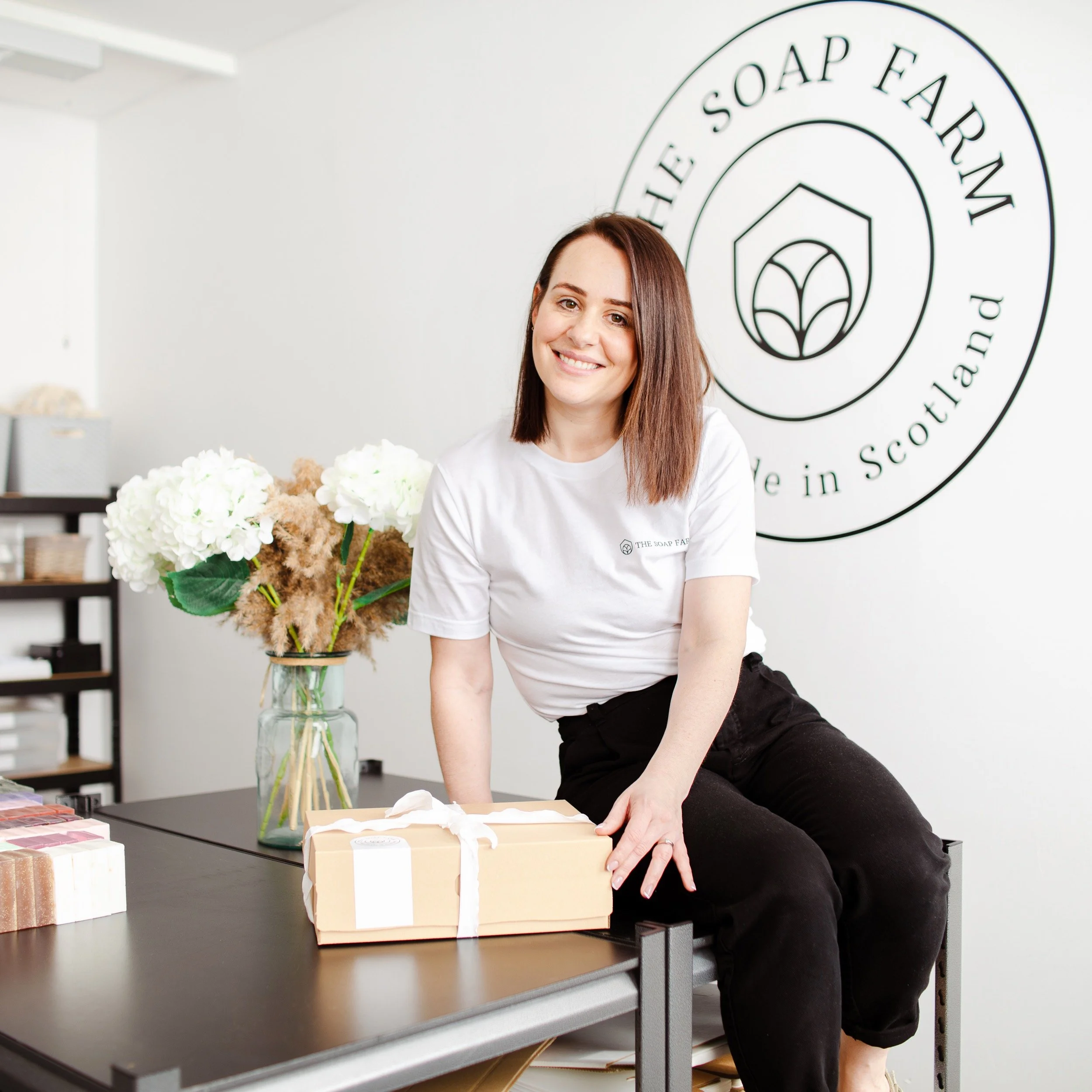 Maxine sits on her workshop table with a gift box of packaged soaps