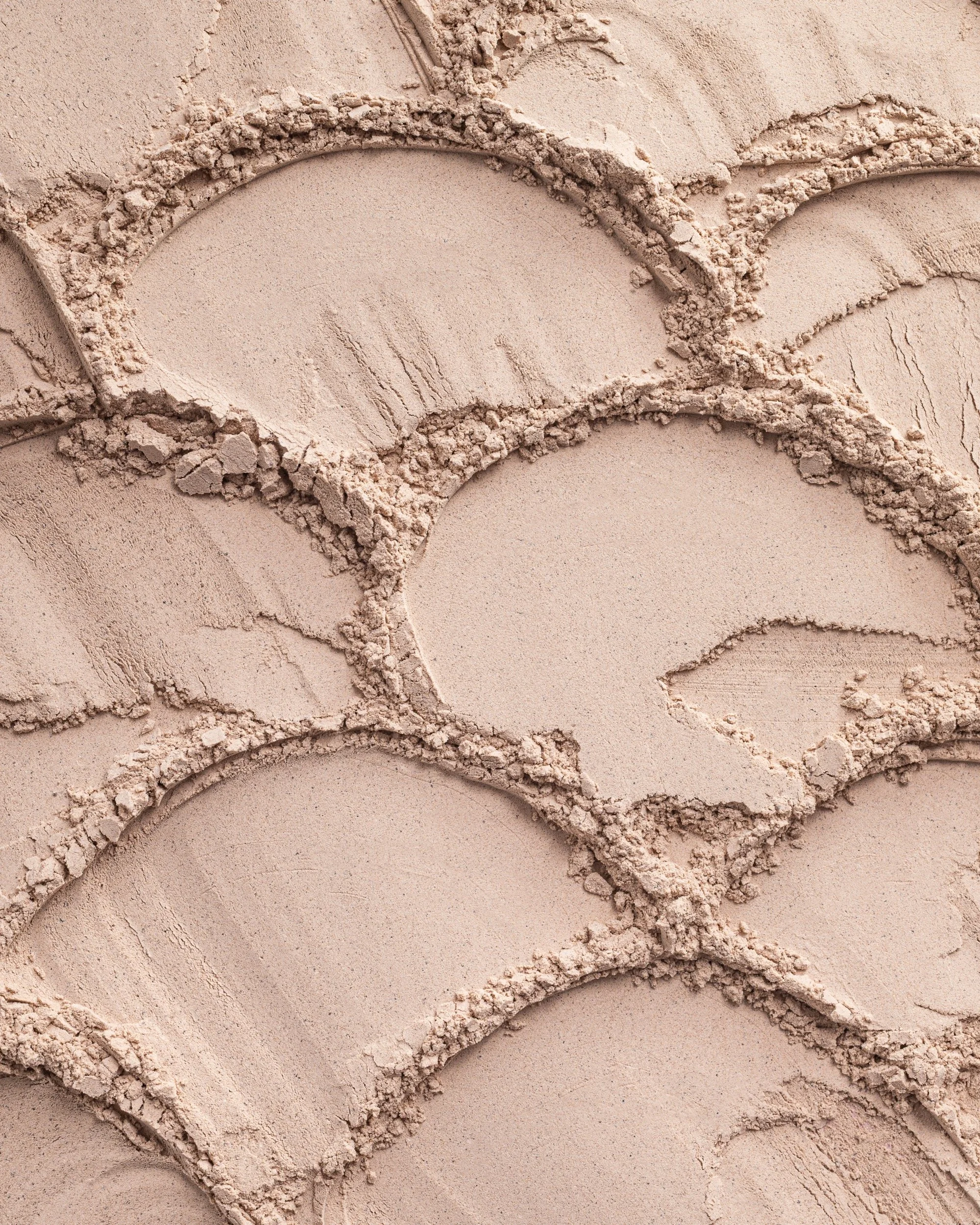 Close-up of several areas of light beige pressed powder makeup, with some parts smoothed out and others with powdery, textured crumbles.