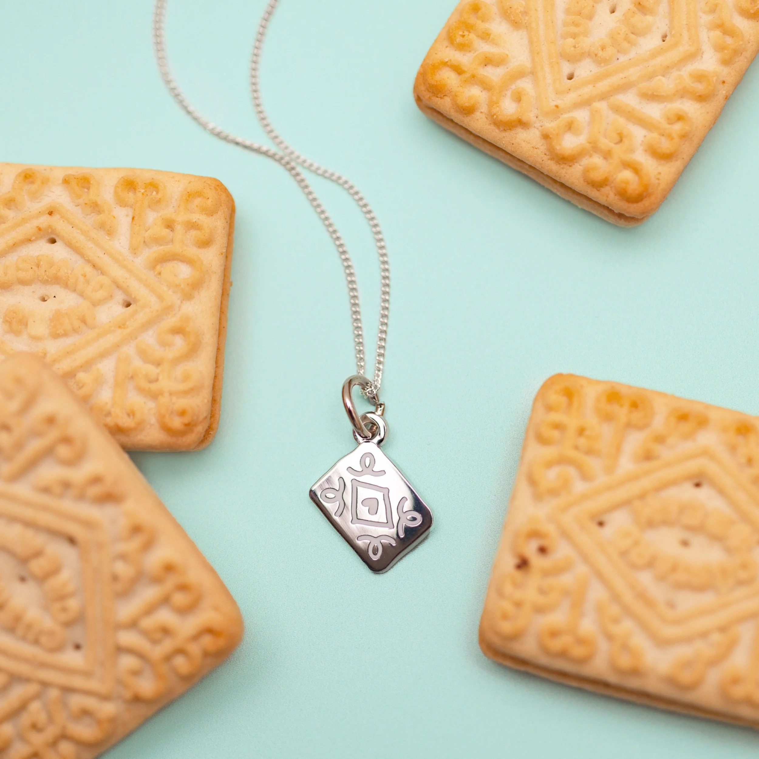 Silver necklace with a custard cream pendant, surrounded by four square biscuits with embossed patterns