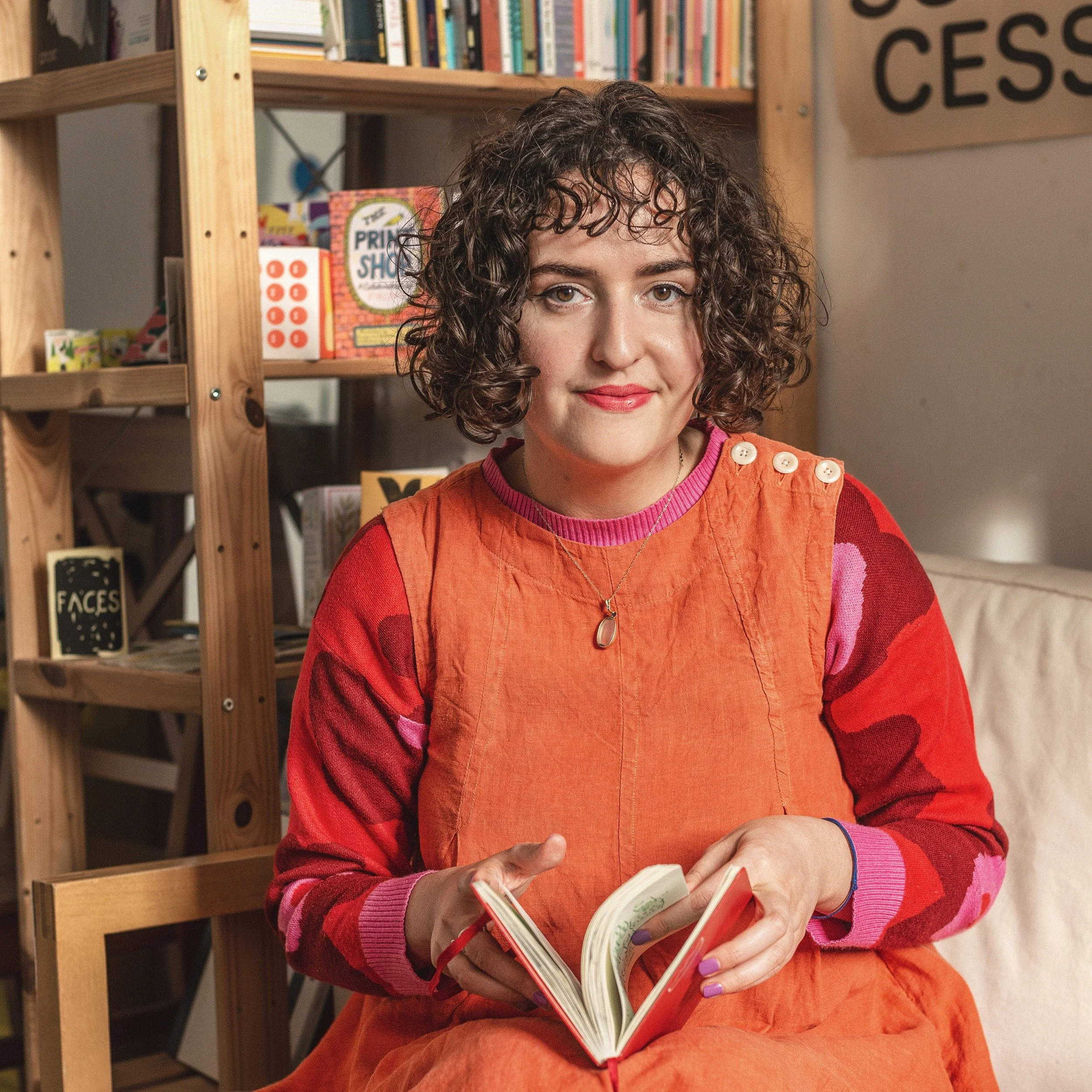 Cara sits in front of a book case, holding her sketchbook