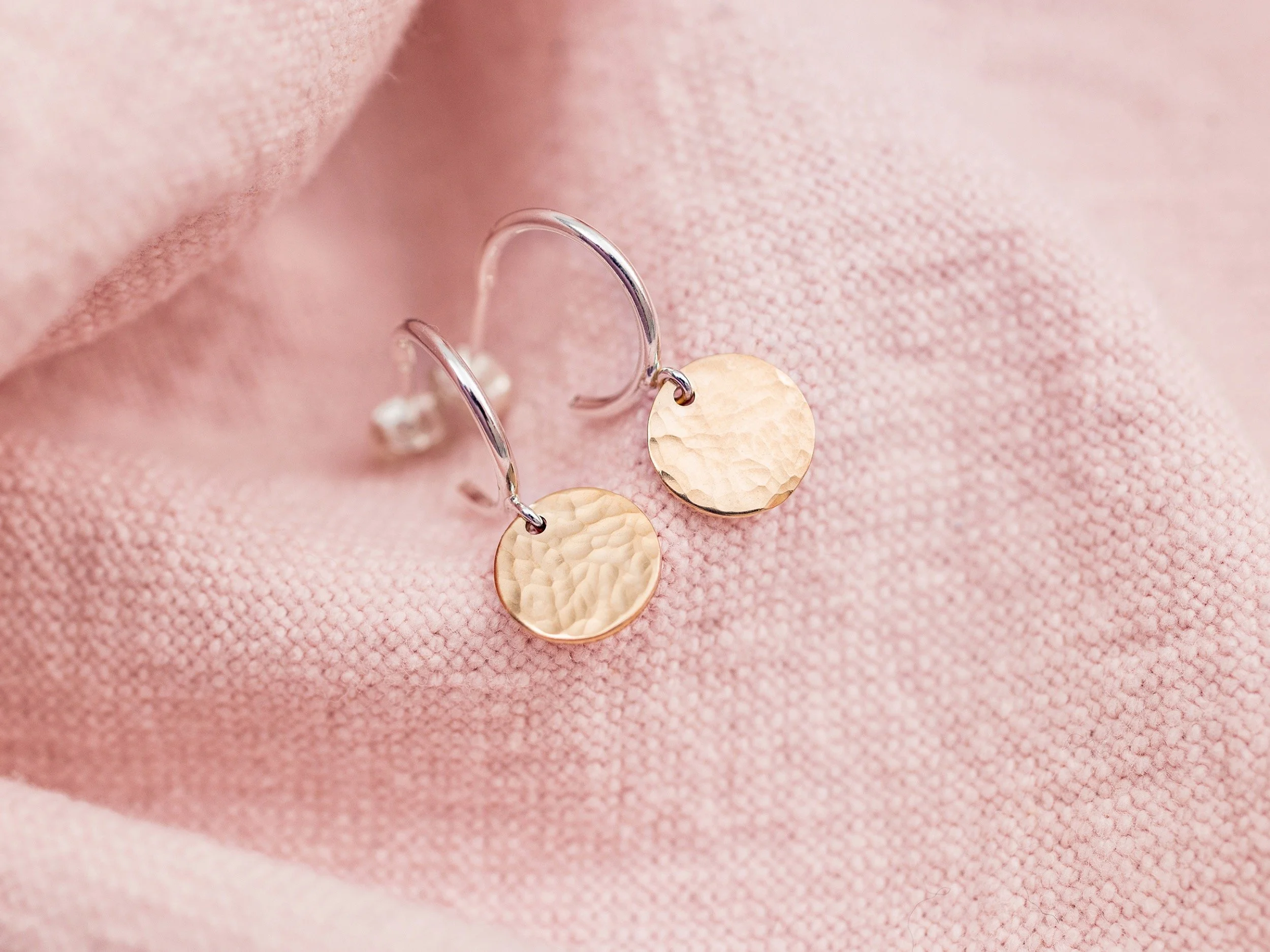 hammered gold earrings are photographed on pink linen