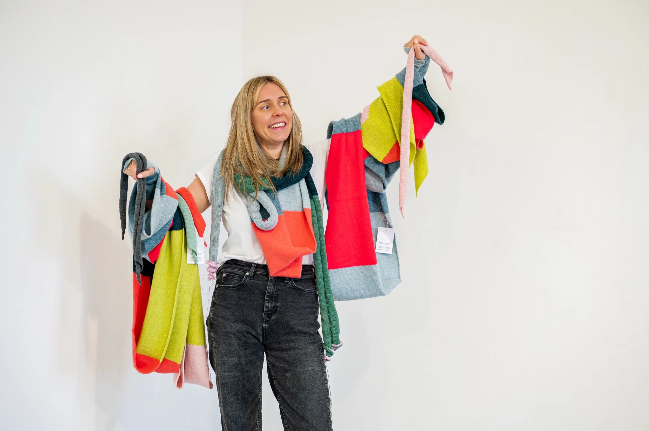 Lyndsey is smiling, wearing lots of colourful knitwear draped around her neck and arms