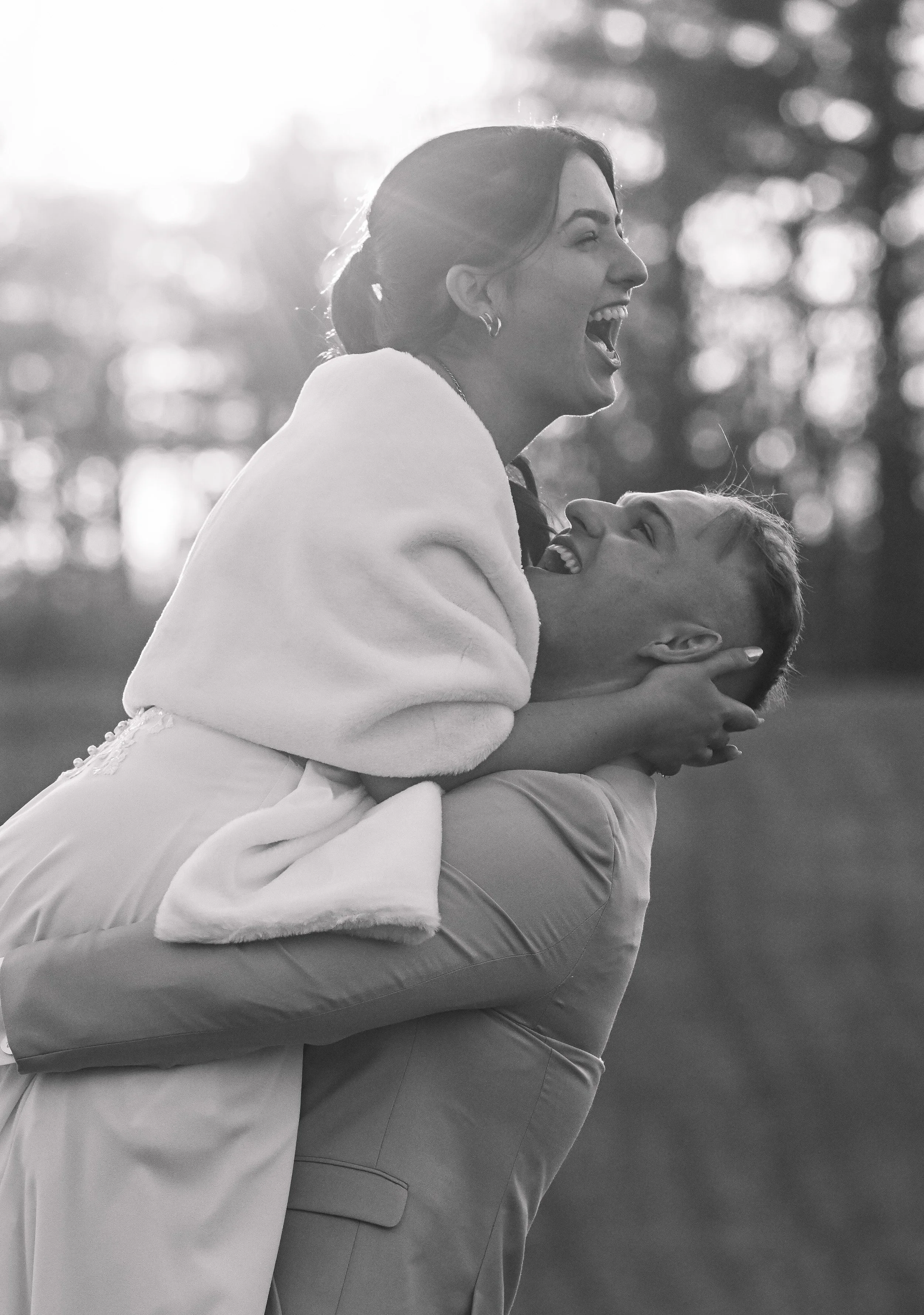 A man lifts a woman in celebration, both smiling and laughing outdoors, black and white photograph.