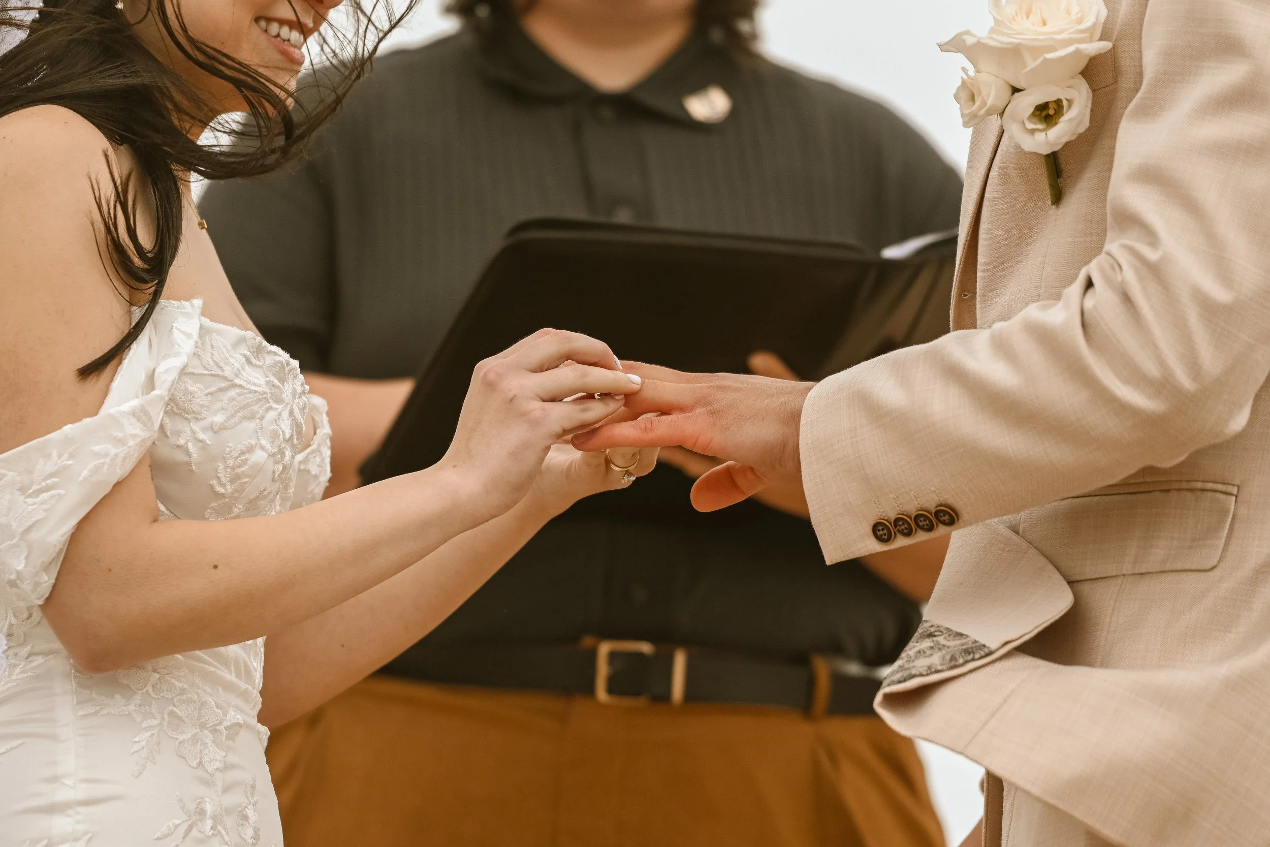A bride and groom holding hands during their wedding ceremony, with an officiant in the background.
