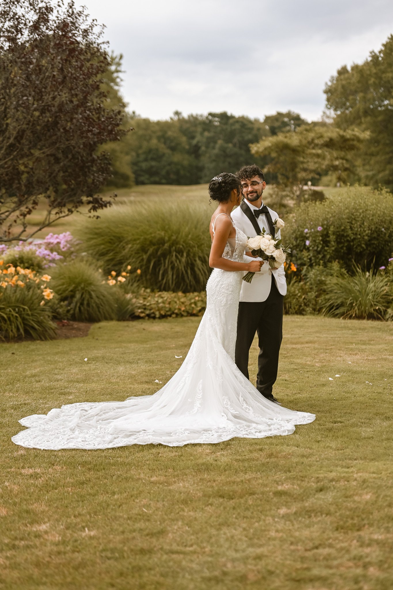 A bride in a white lace wedding dress is smiling and holding her hand to he grooms arm looking into his eyes, Holding her bouquet while surrounded by the beautiful Cyprian Keys Golf Club venue
