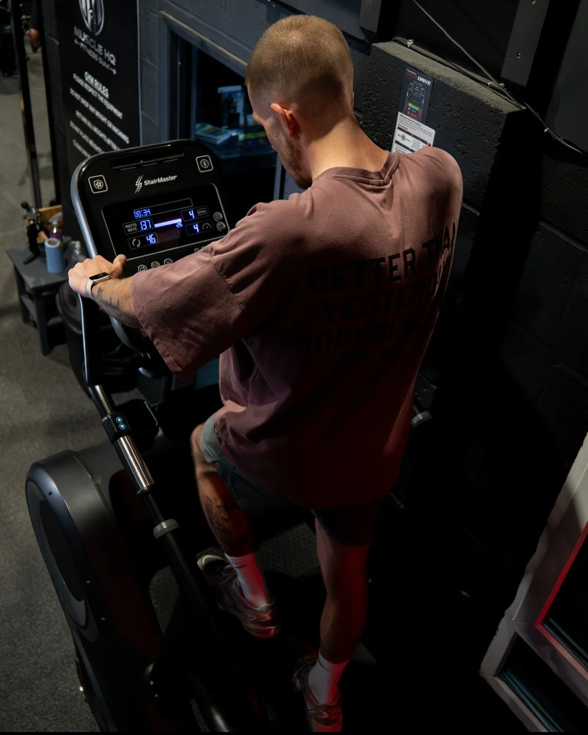 Man using a stair stepping machine in a gym, wearing a brown t-shirt.