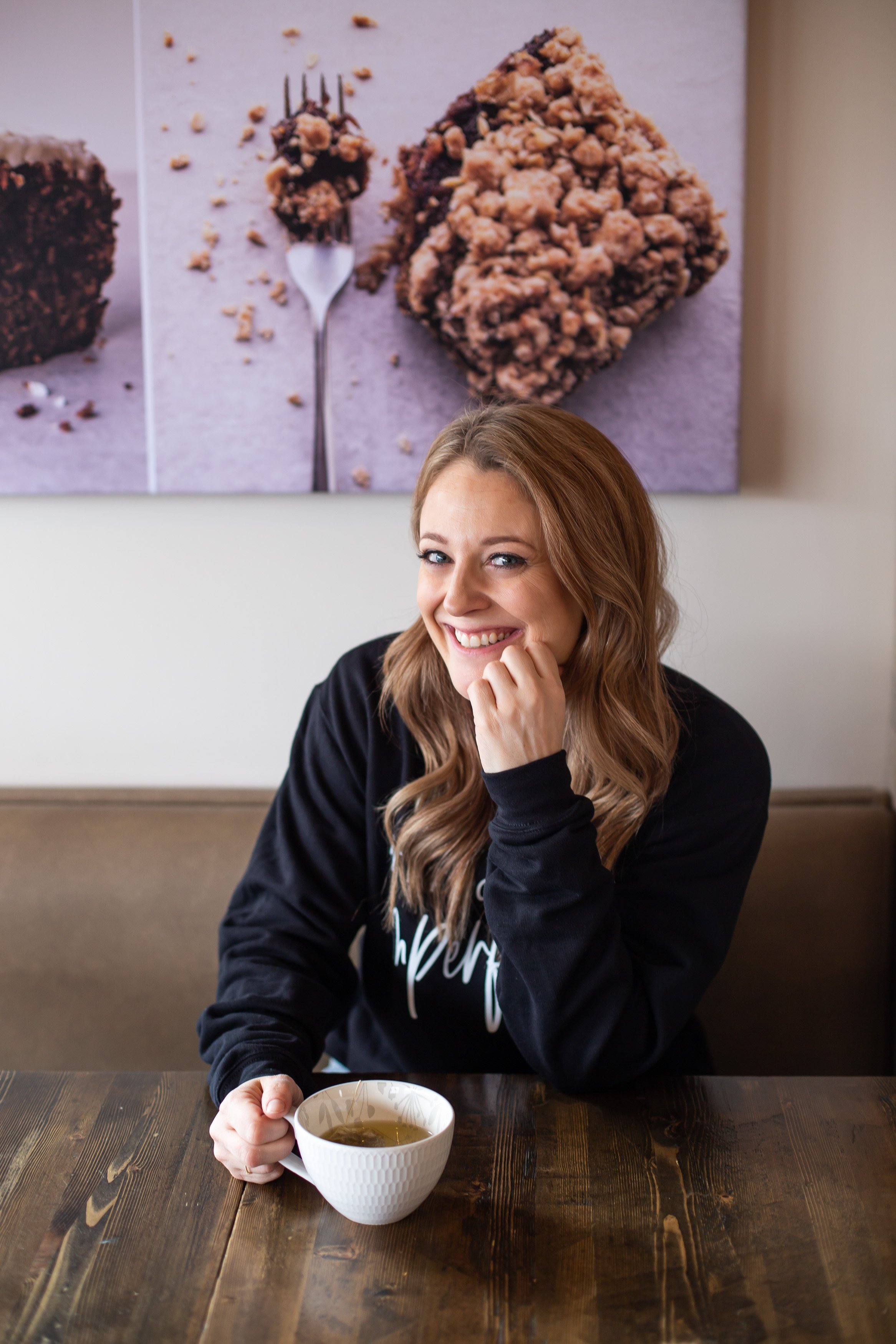 woman in coffee shop holding her mug and smiling at camera in black sweater