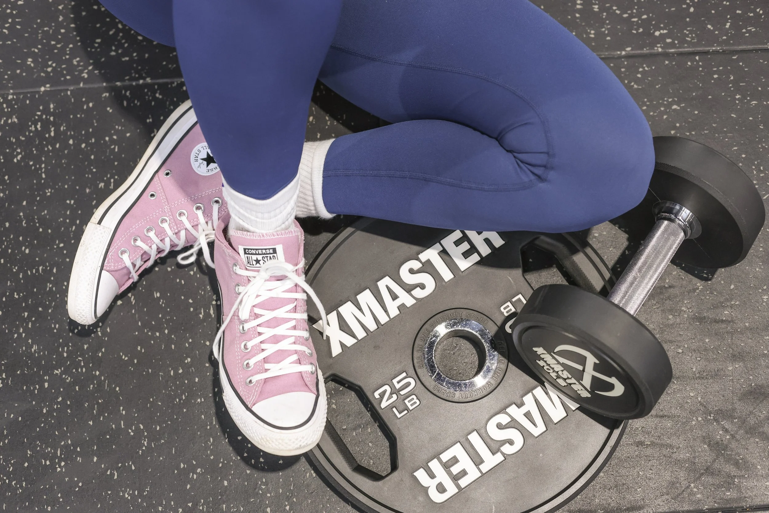 woman in blue leggies sitting on floor with a plate and dumbells and pink converse shoes on