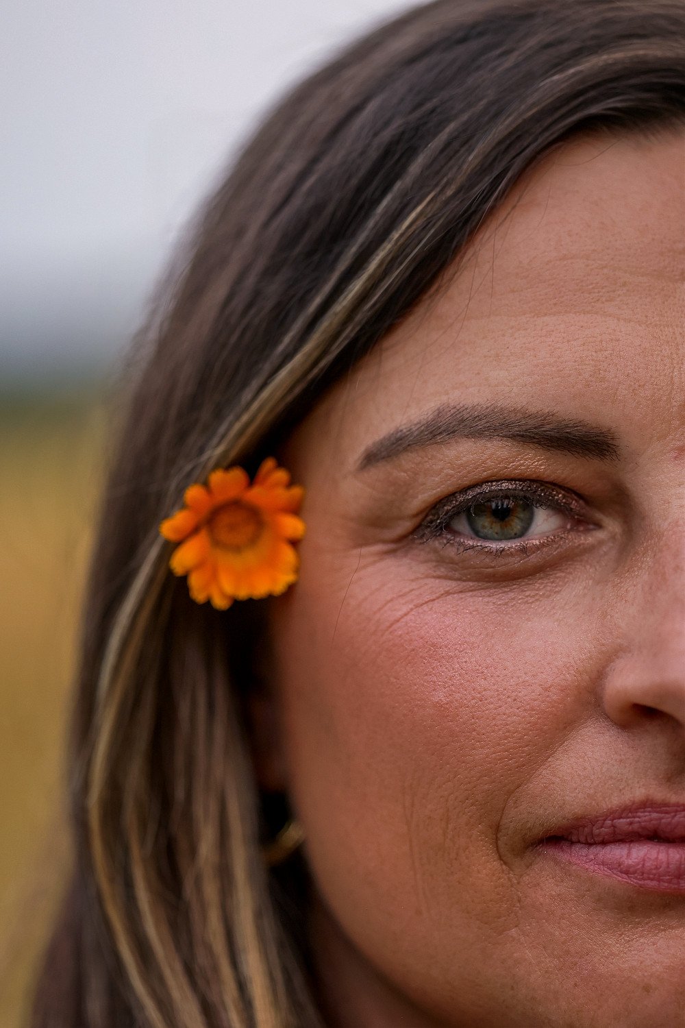 up close of womand face and eye with orange flower in her hair