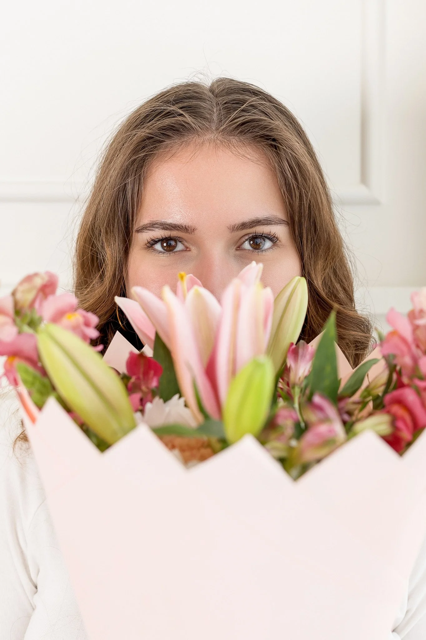 woman holding flowers to her face with eyes peeking over and clear in view