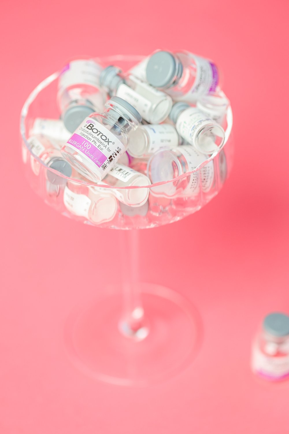 bottles of botox in martini glass in front of a pink backdrop